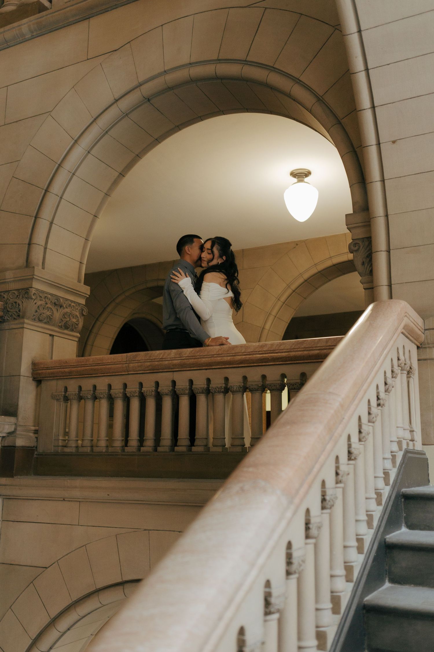 Couple sharing romantic kiss on balcony of elegant stone building staircase.
