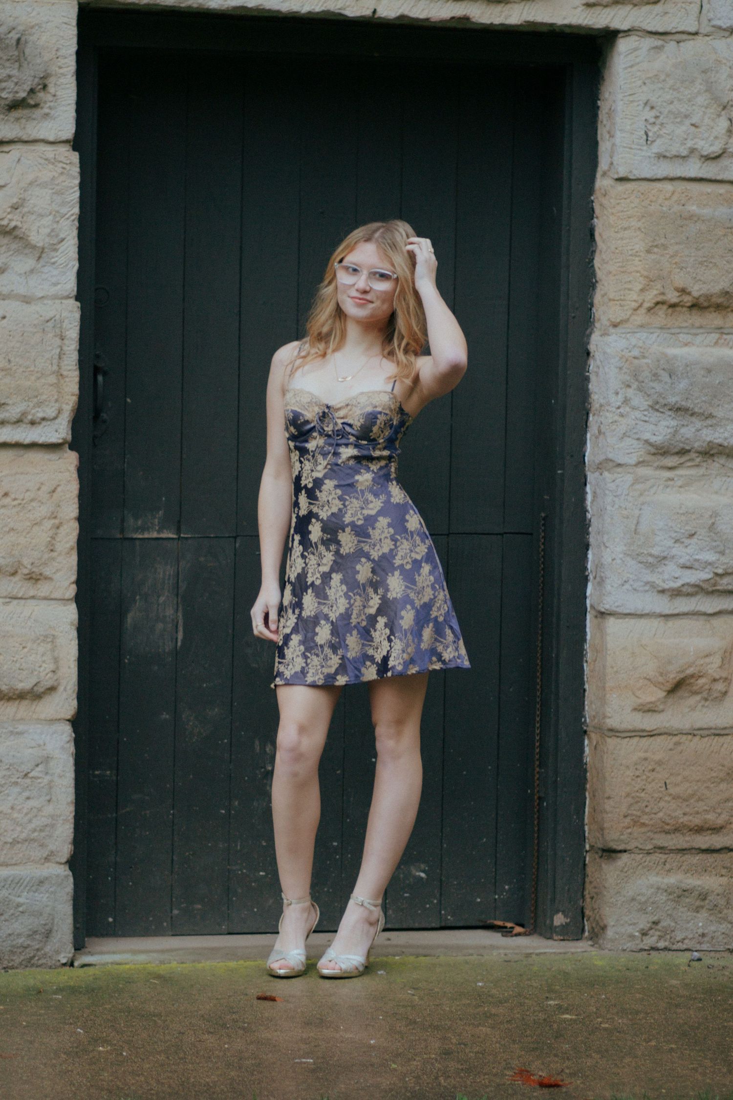 Blonde teen girl in floral strapless dress posing in front of a dark green wooden door.
