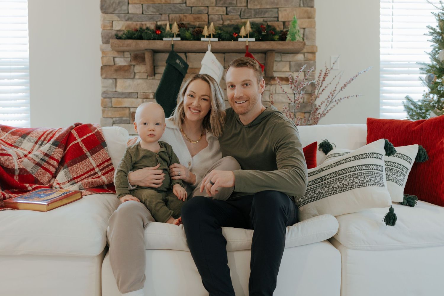 Smiling family with mother, father, and baby in green outfit on white couch at Christmas in Pittsburgh