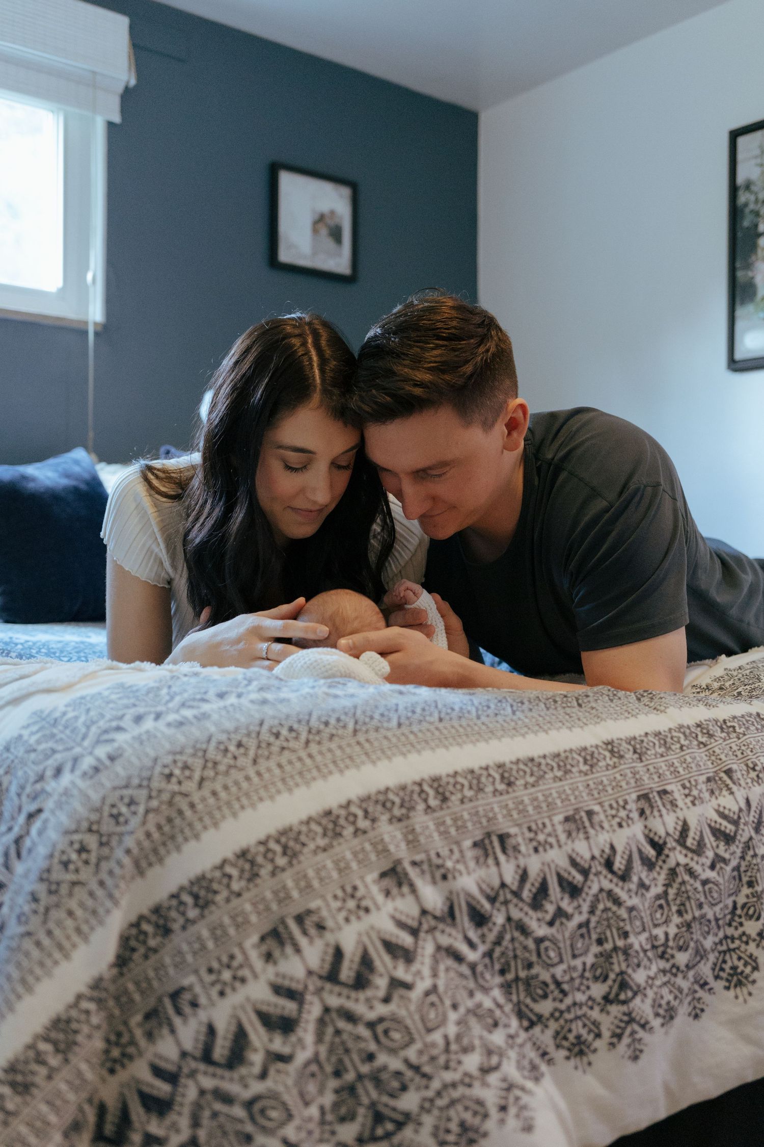 New parents lying on bed gazing lovingly at their newborn baby together.