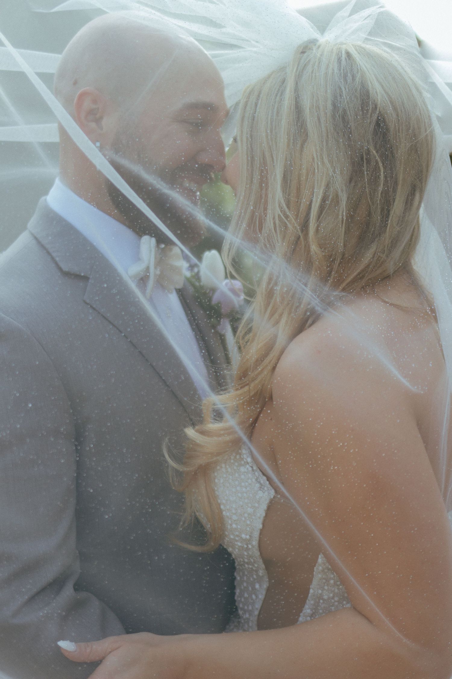 Bride and groom sharing an intimate moment under a flowing veil on their wedding day.