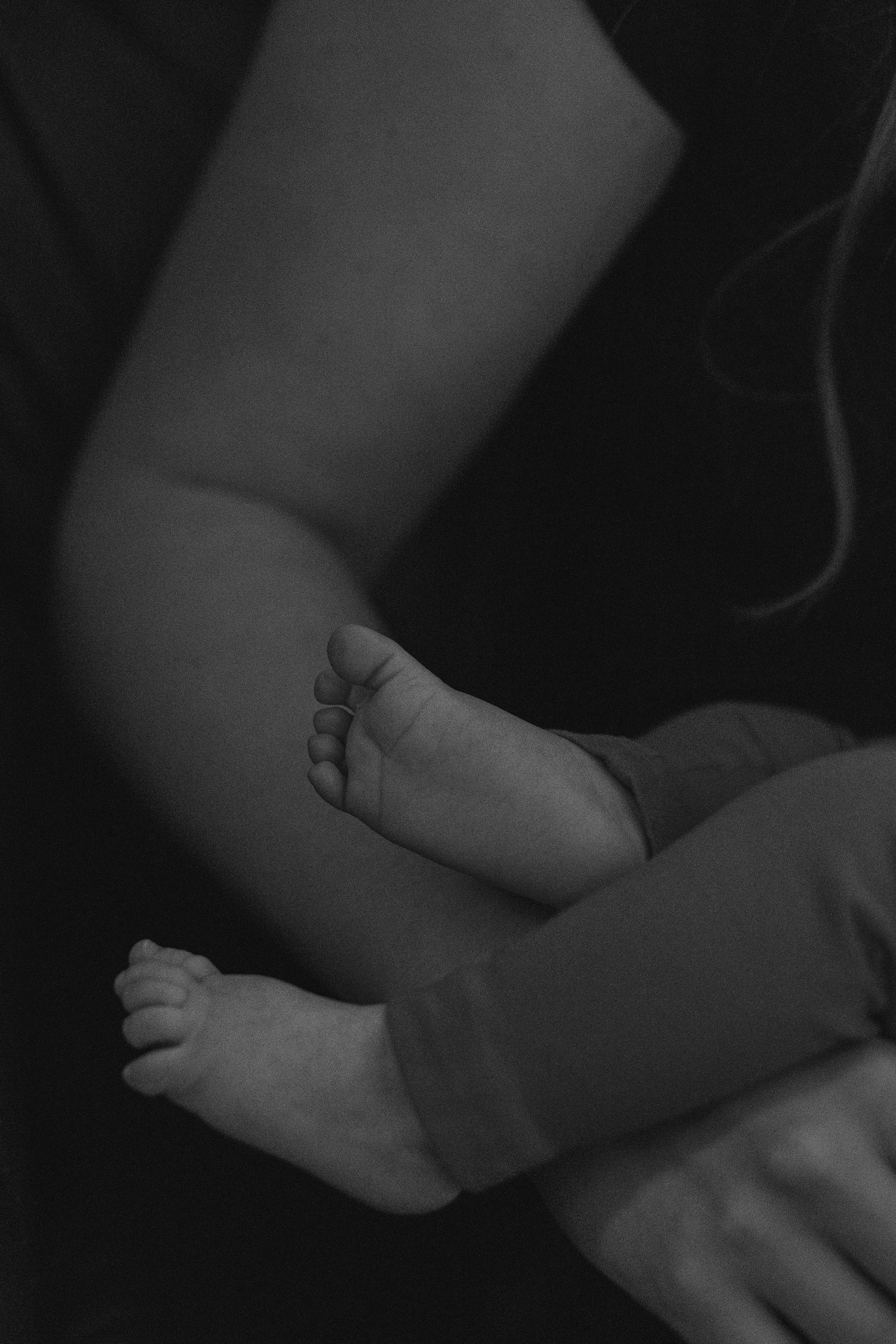 A black and white close-up photo capturing the tiny feet of a newborn baby resting on an adult arm.