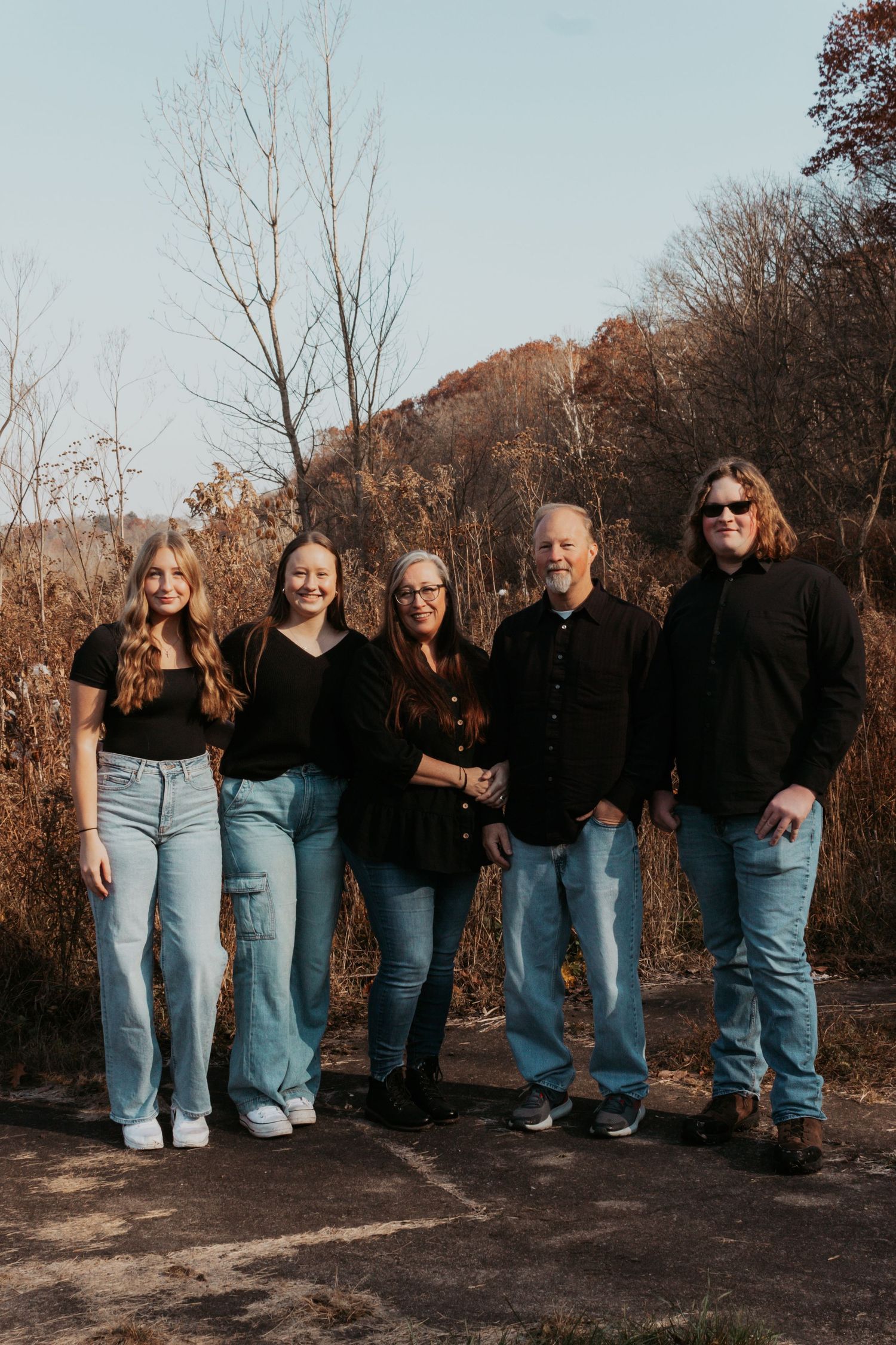 Family of five in matching black tops and jeans posing outdoors during autumn.