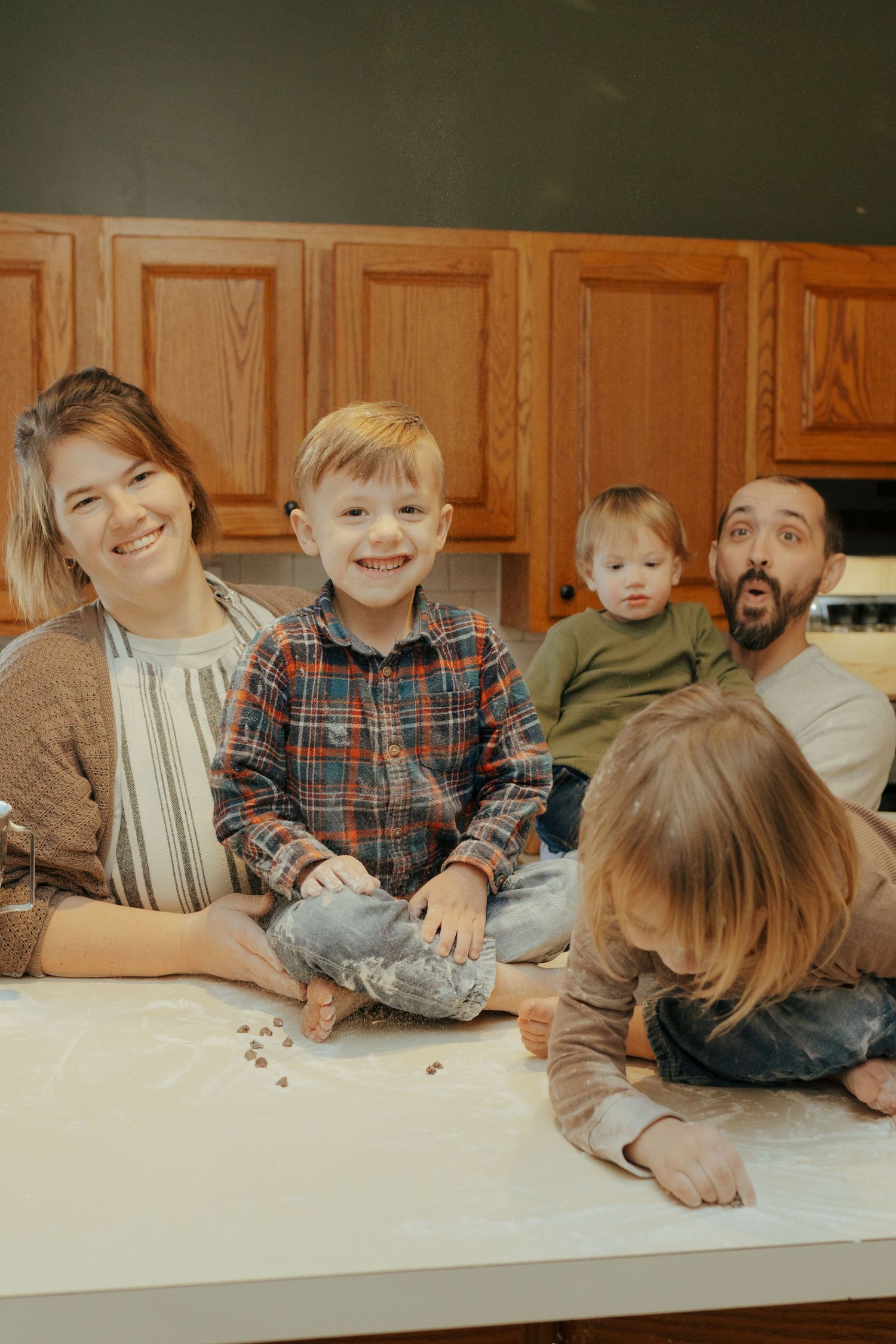 Joyful family of five sitting together on kitchen counter covered in flour during baking session.