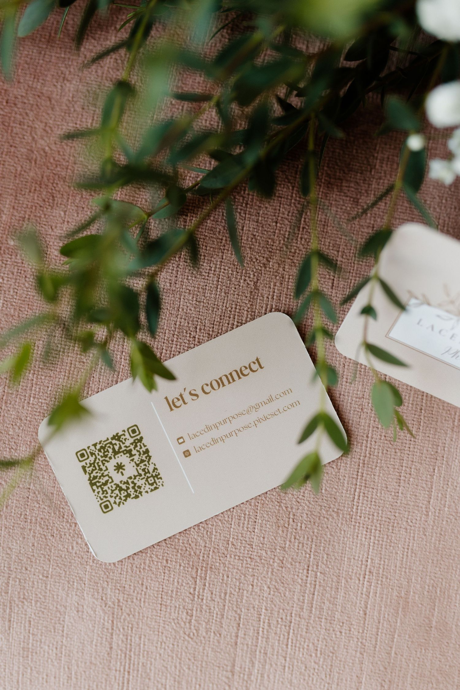 Beige business card with QR code reading lets connect surrounded by green leaves.