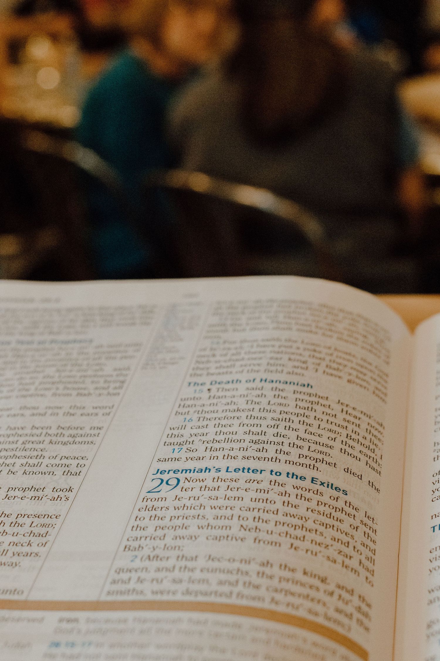An open Bible displays Jeremiah chapter 29 with a softly blurred congregation visible in the background.