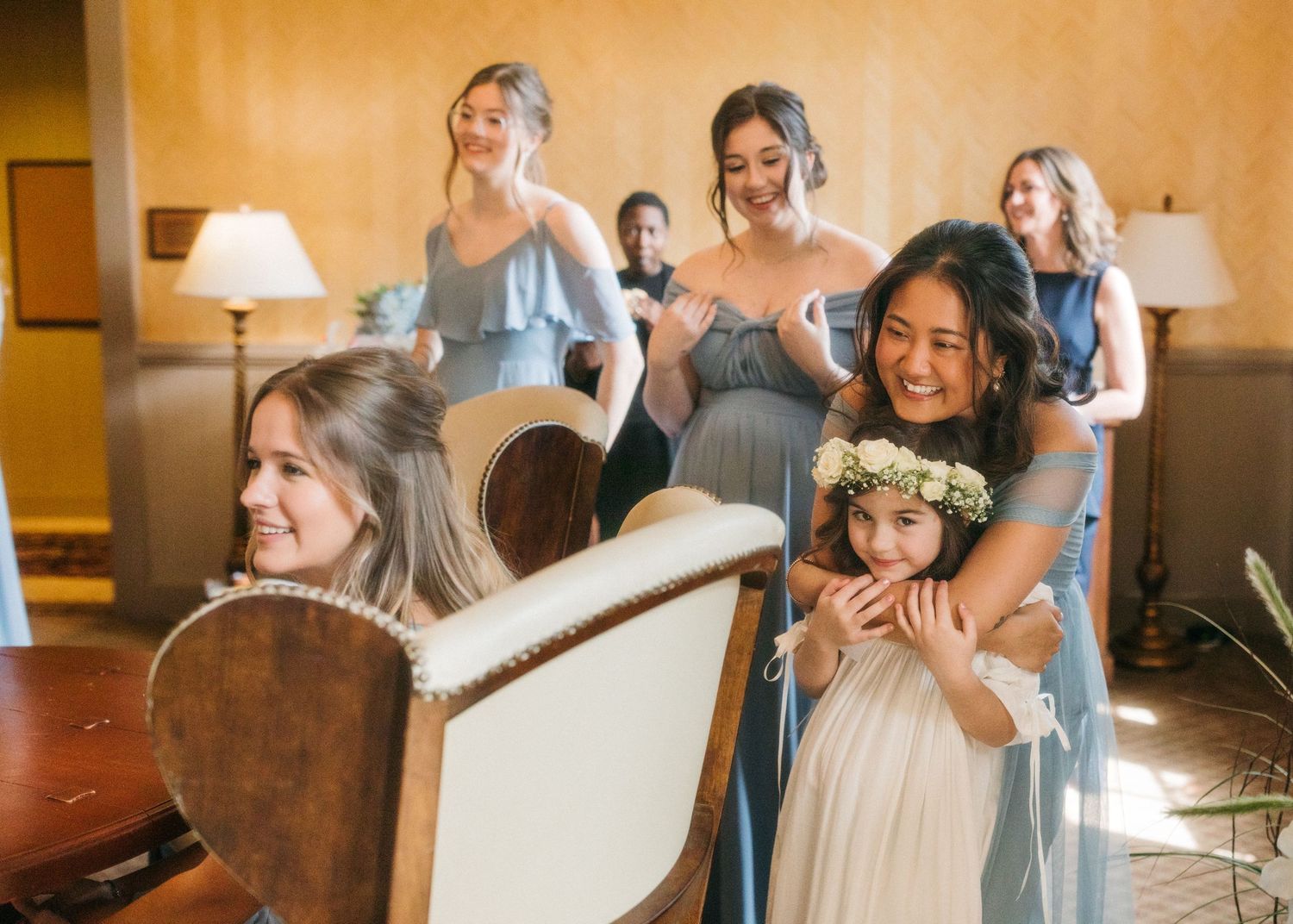 Bridesmaids and flower girl share an emotional and joyful moment during wedding preparations indoors.