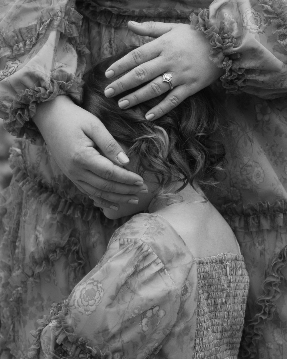Black and white close-up of mother's hands with ring gently touching child's hair in flowing dress.