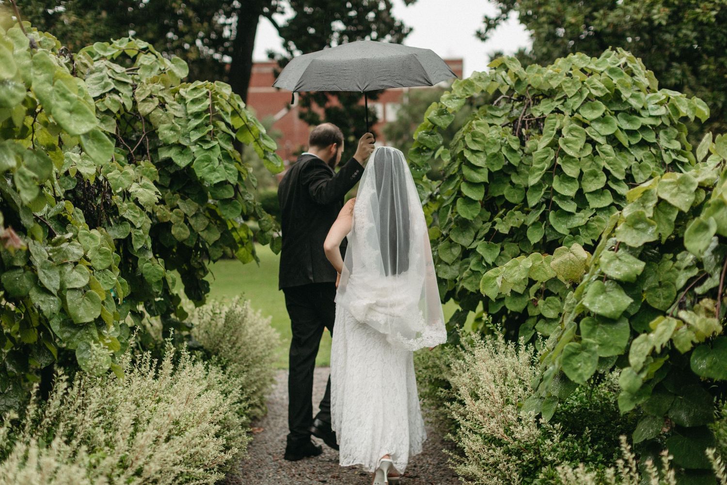 Bride and groom share a romantic moment under an umbrella in a lush garden.