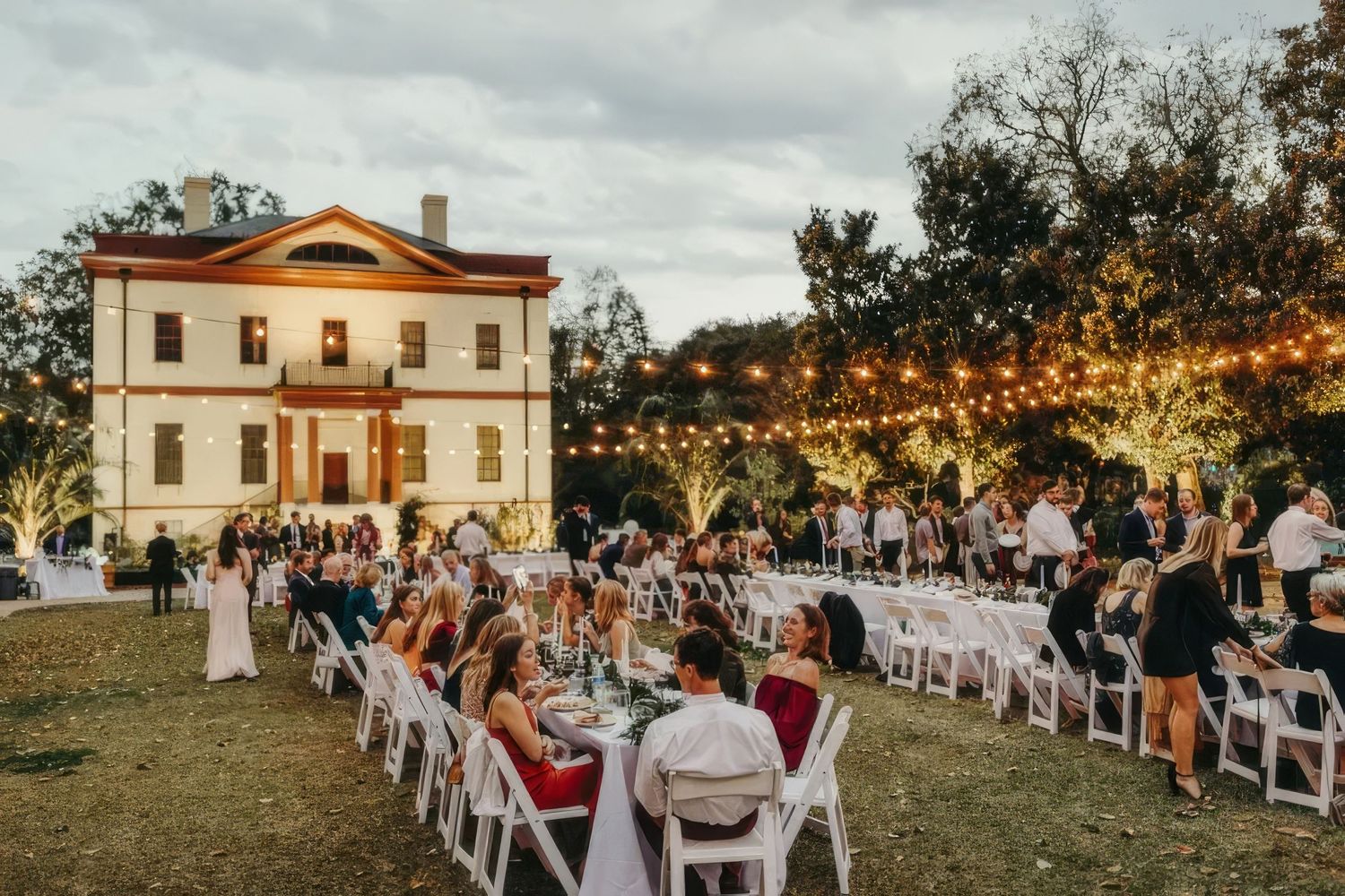 Elegant outdoor wedding reception with long tables and string lights in front of historic venue.