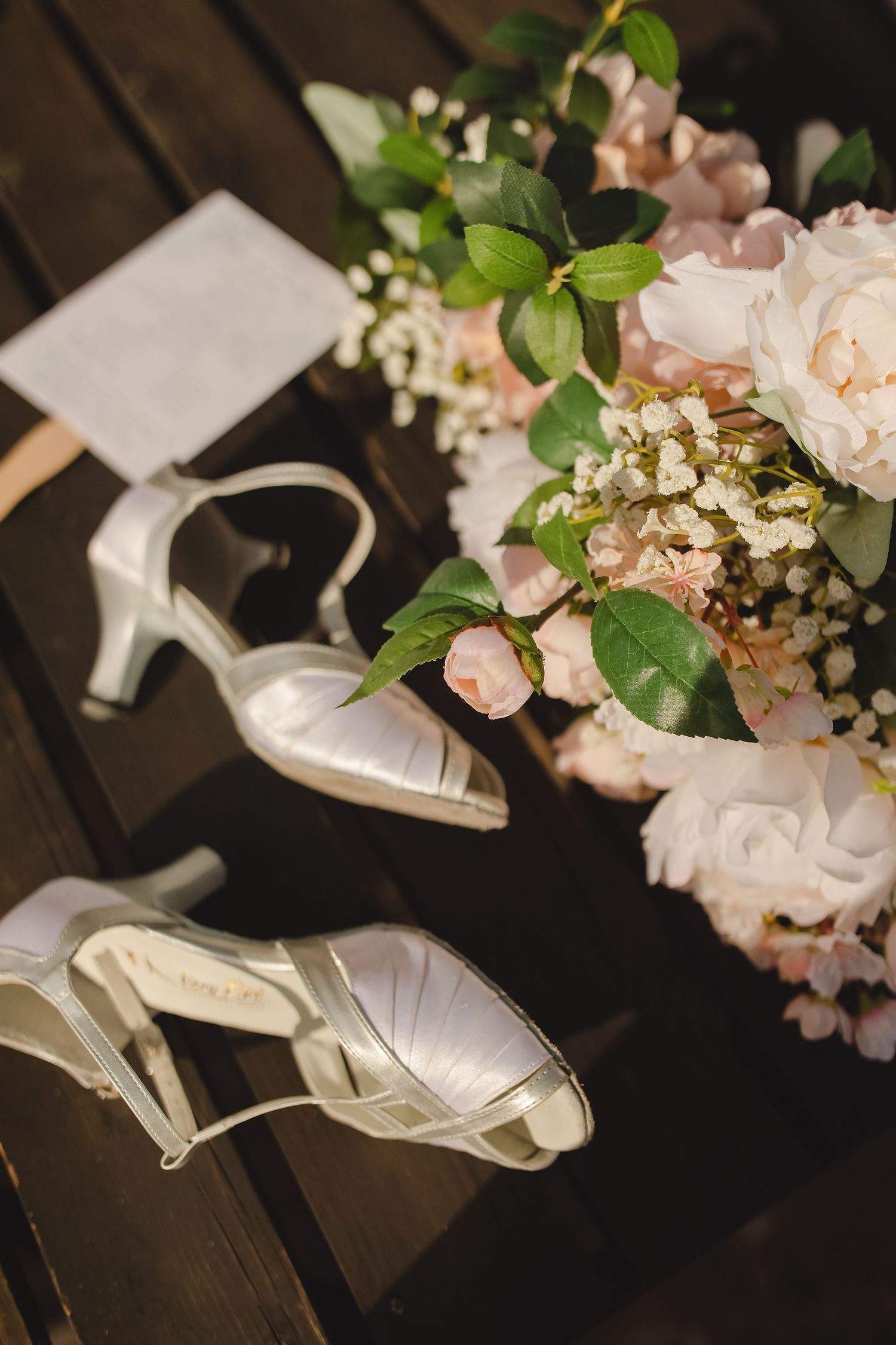 White satin wedding heels placed beside a blush pink floral bridal bouquet.