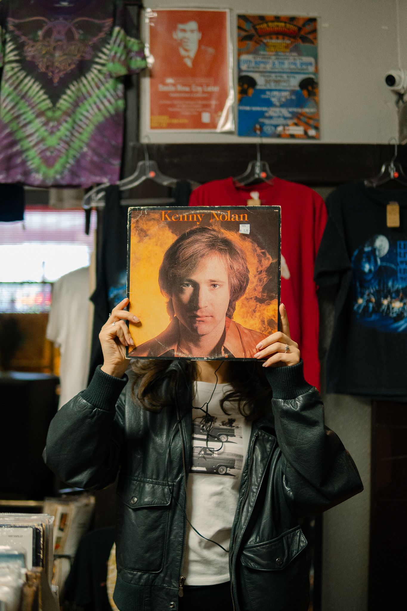Someone holds up a Kenny Wayne Shepherd vinyl album cover while wearing a black leather jacket in what appears to be a record store.
