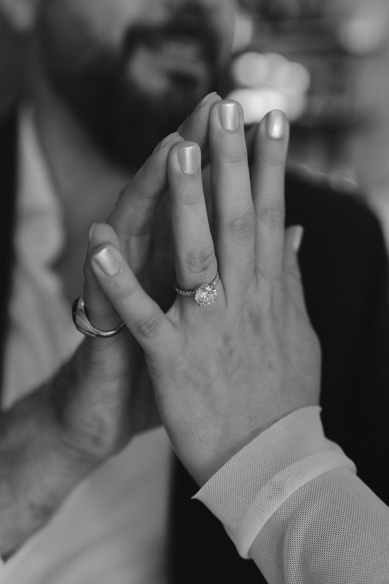 Black and white photo of couple holding hands showing engagement ring and wedding band.