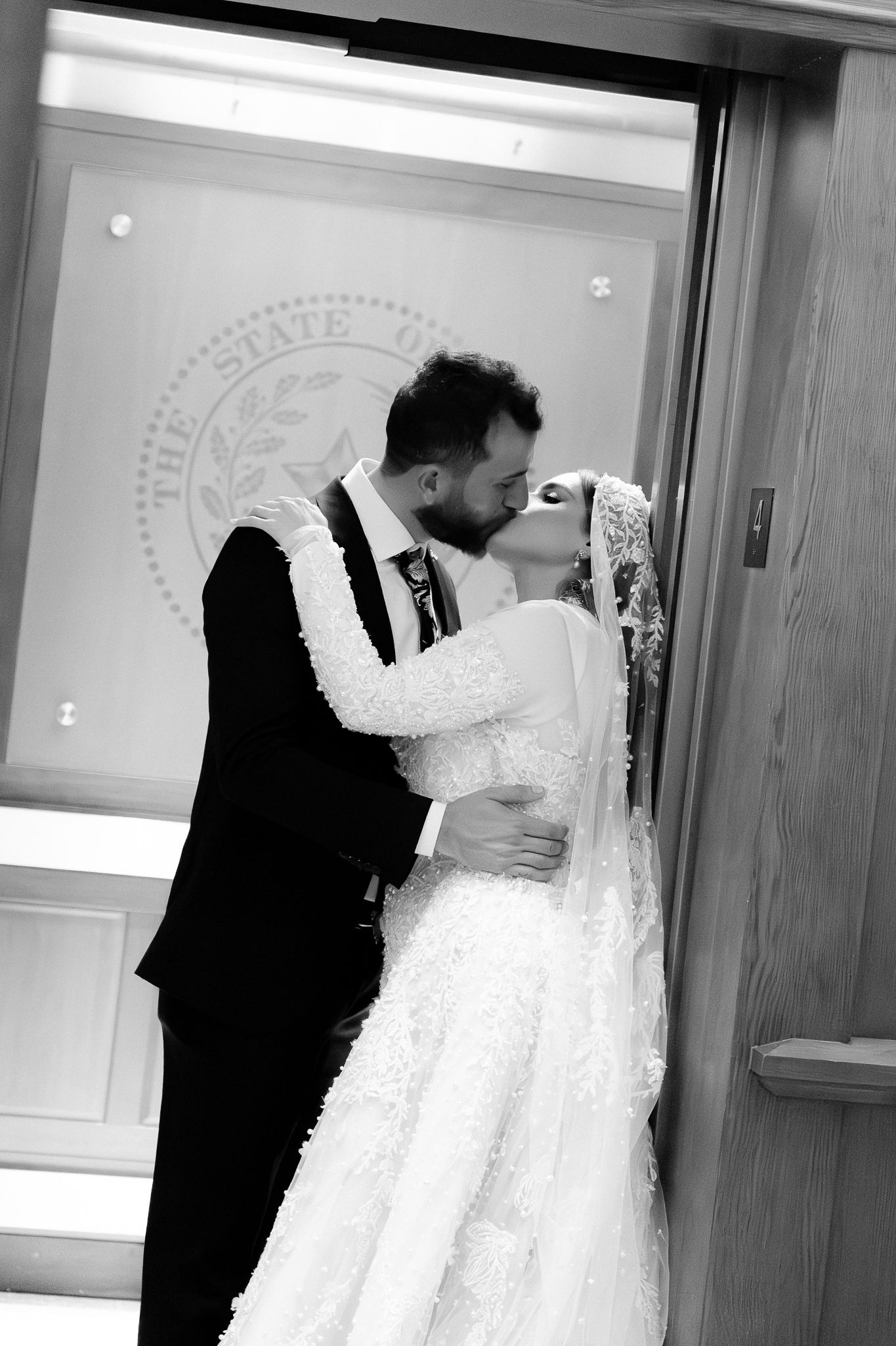 A couple shares an intimate moment in black and white while looking at a wedding dress displayed on a hanger.