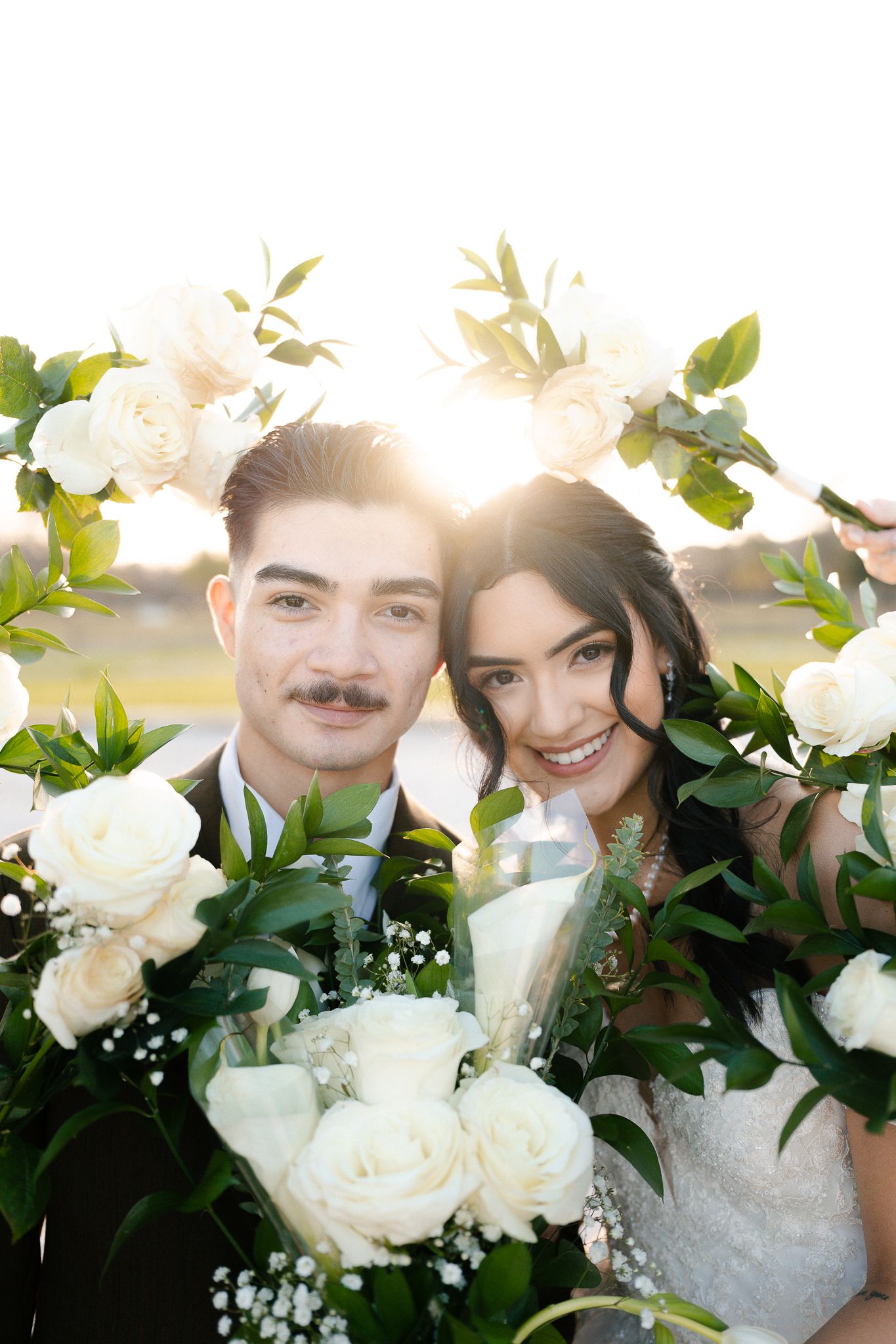 White roses frame a romantic wedding photo with soft sunlight glowing through the flowers.