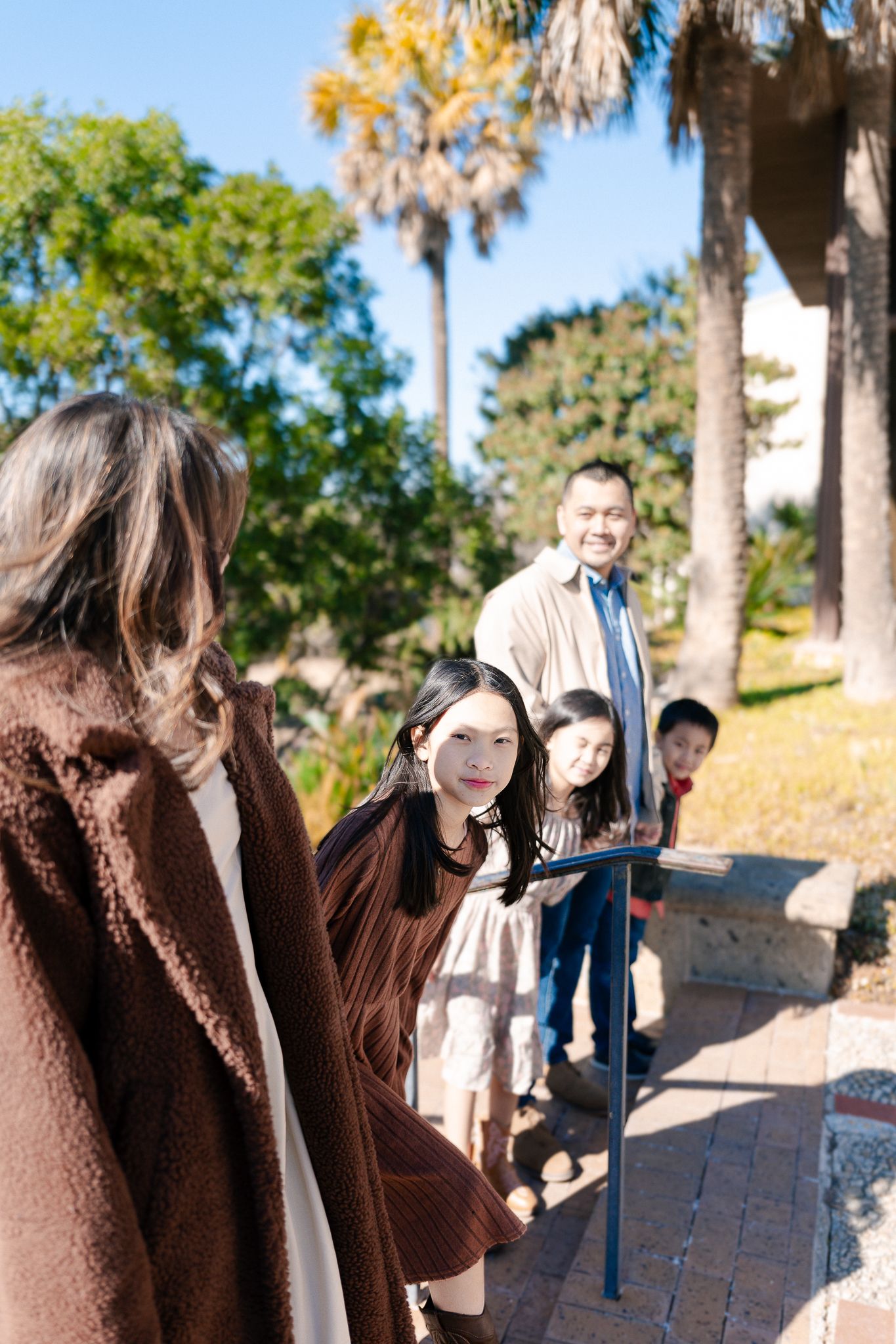 A group of people walking up outdoor stairs on a sunny day with palm trees and greenery in the background.