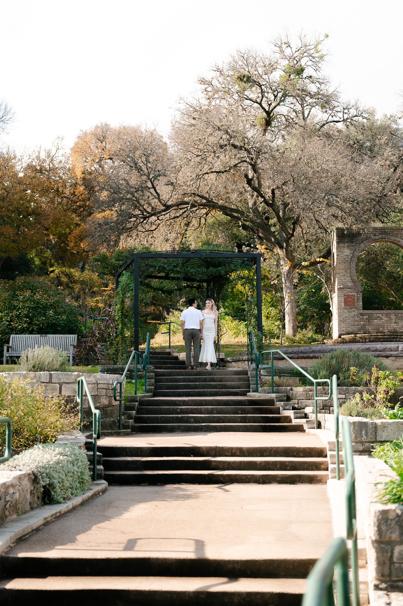 Stone steps with metal handrails lead up through a garden path surrounded by blooming trees and landscaping.