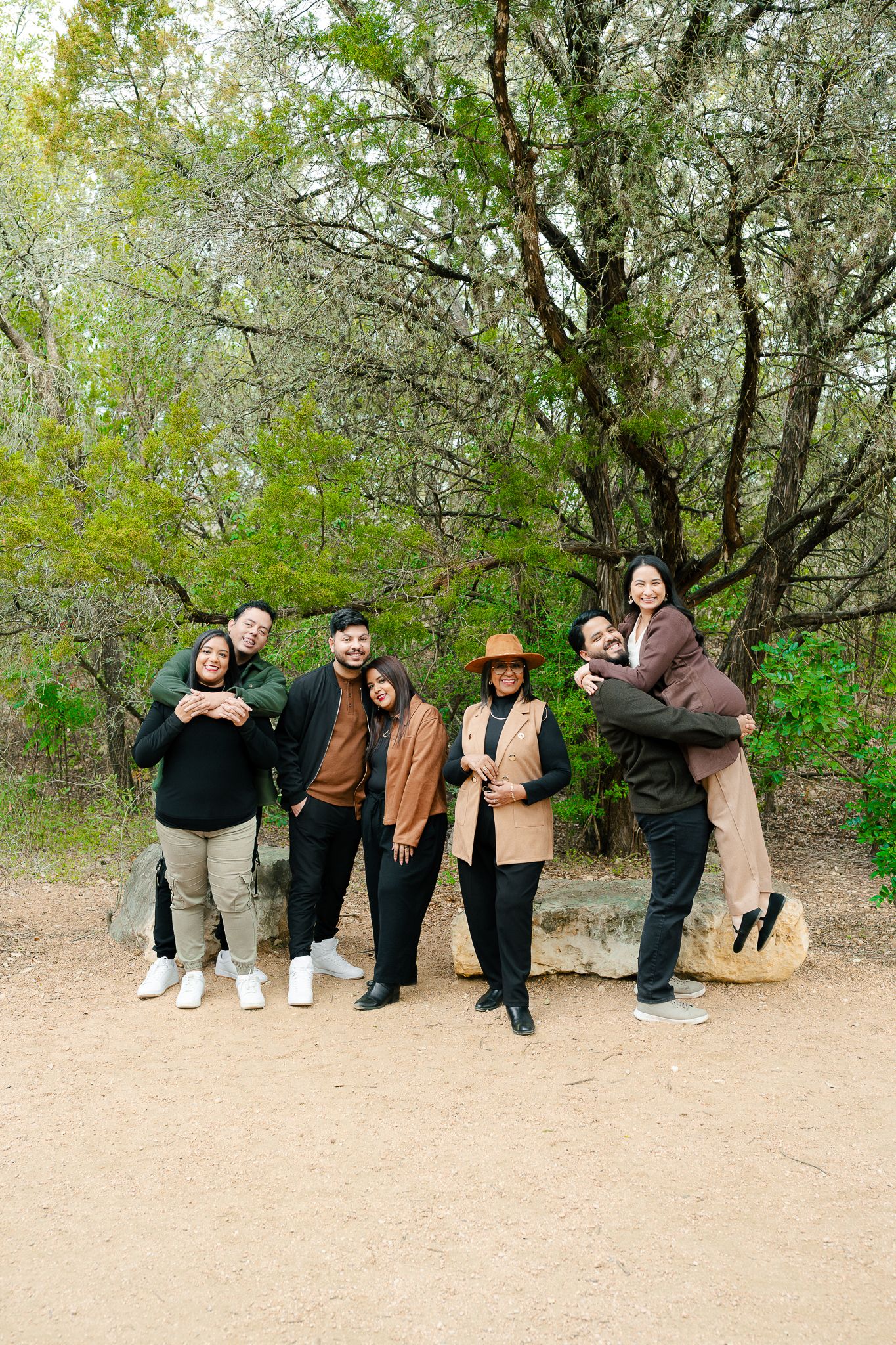 A group of people pose playfully in front of trees and bushes in a sequence of four connected photos.