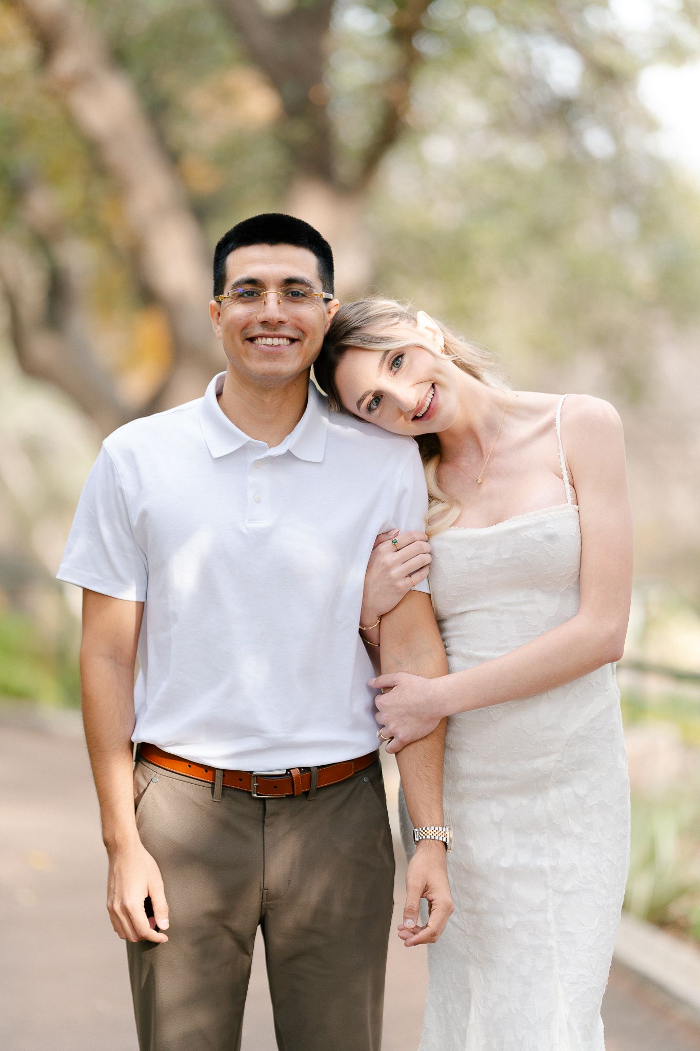 A playful couple in white and khaki poses together in a natural outdoor setting.