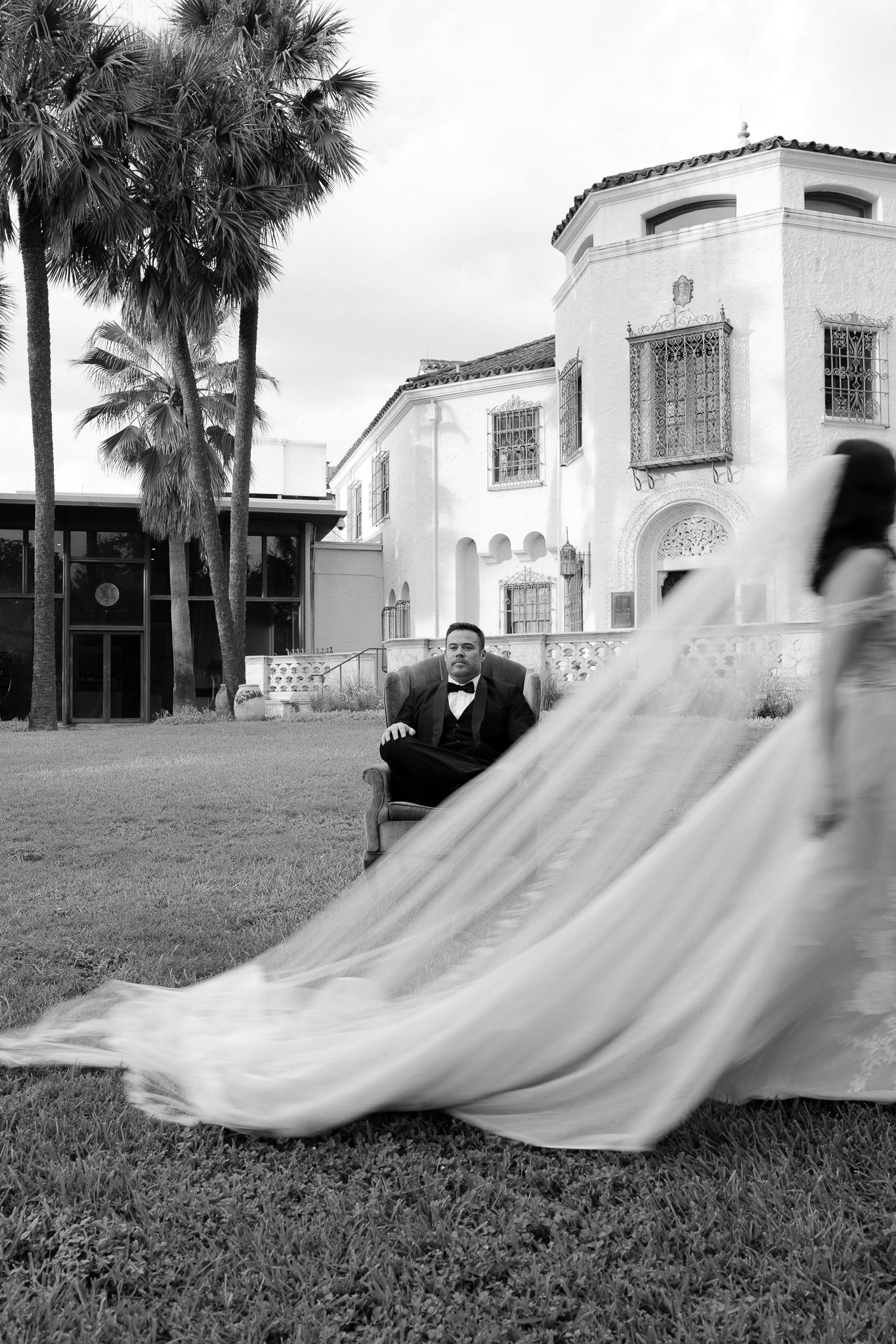 A sequence of black and white photos showing a flowing white wedding dress moving across grass in front of a Spanish-style building.
