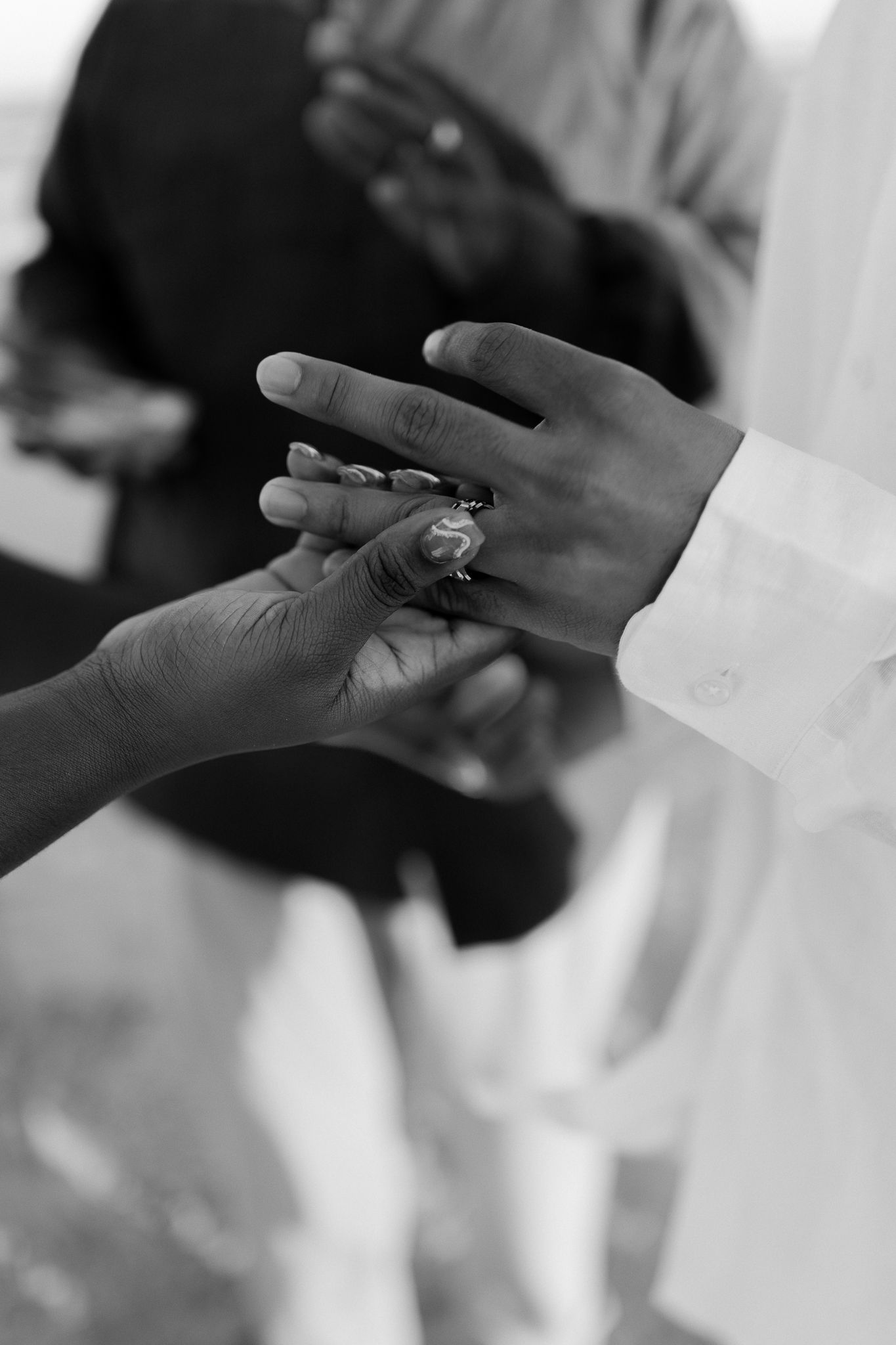 A black and white photograph capturing the intimate moment of placing a wedding ring on a finger during a ceremony.