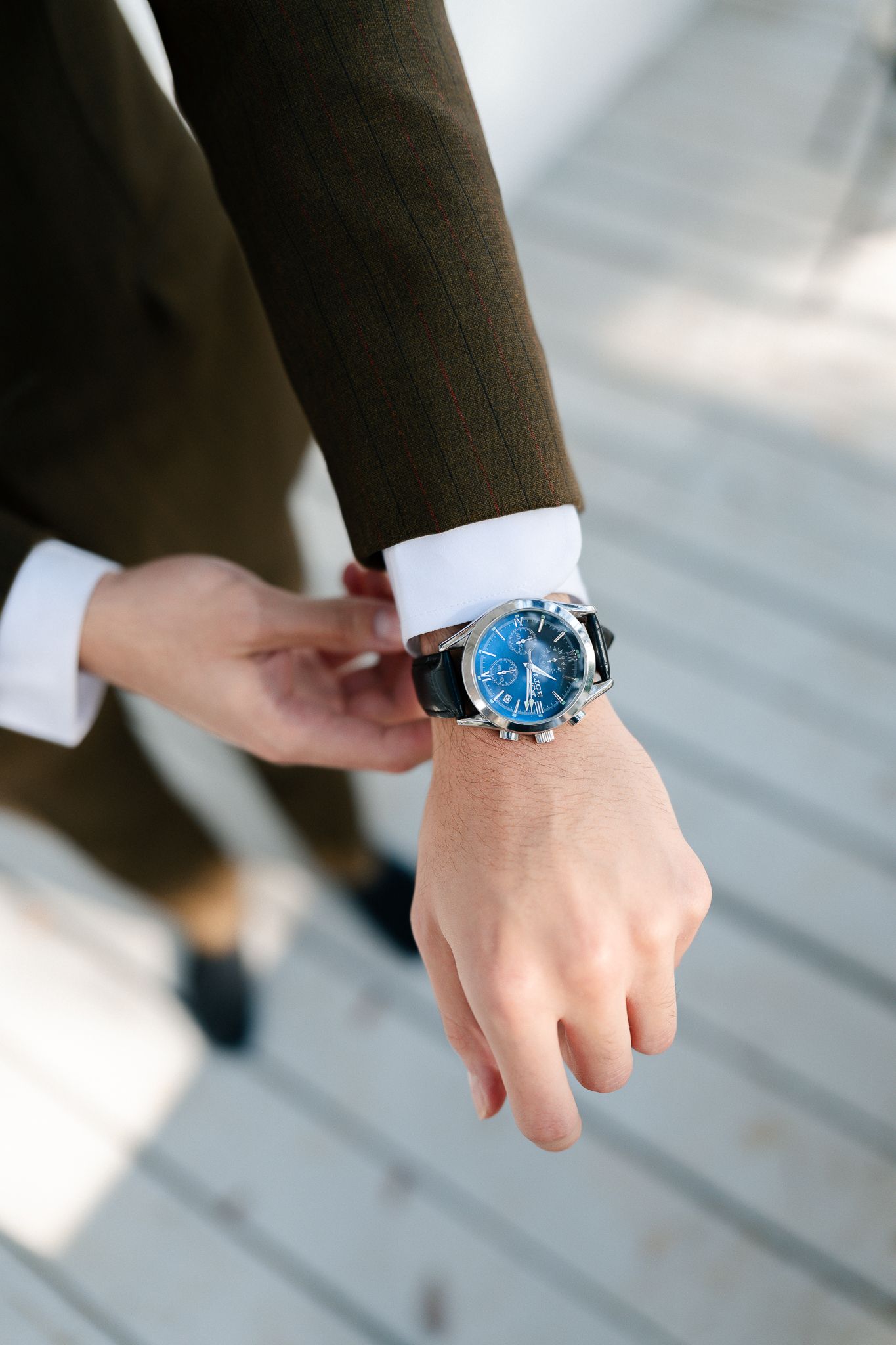 Close-up view of a wrist wearing a blue-faced watch with brown leather strap against a light background.