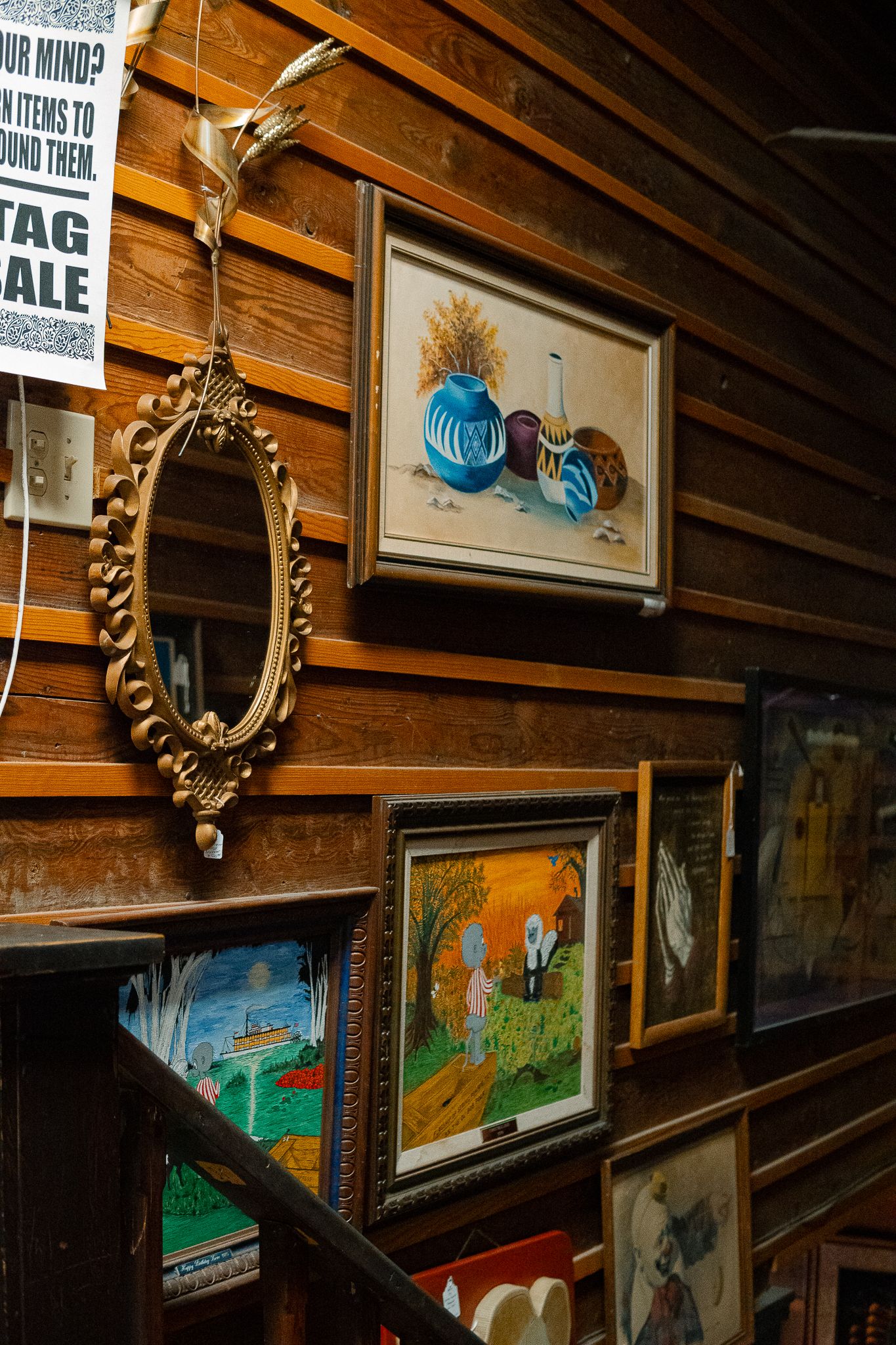 Vintage artwork and framed pieces hang on rustic wooden walls in a dimly lit gallery-style display.