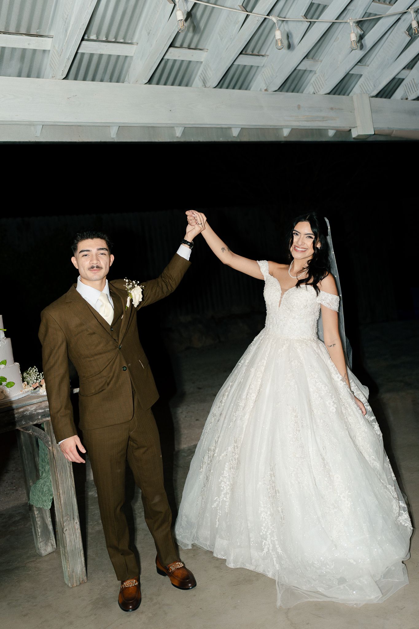 A couple in wedding attire dances together on a beach at night, with the bride in a flowing white gown.