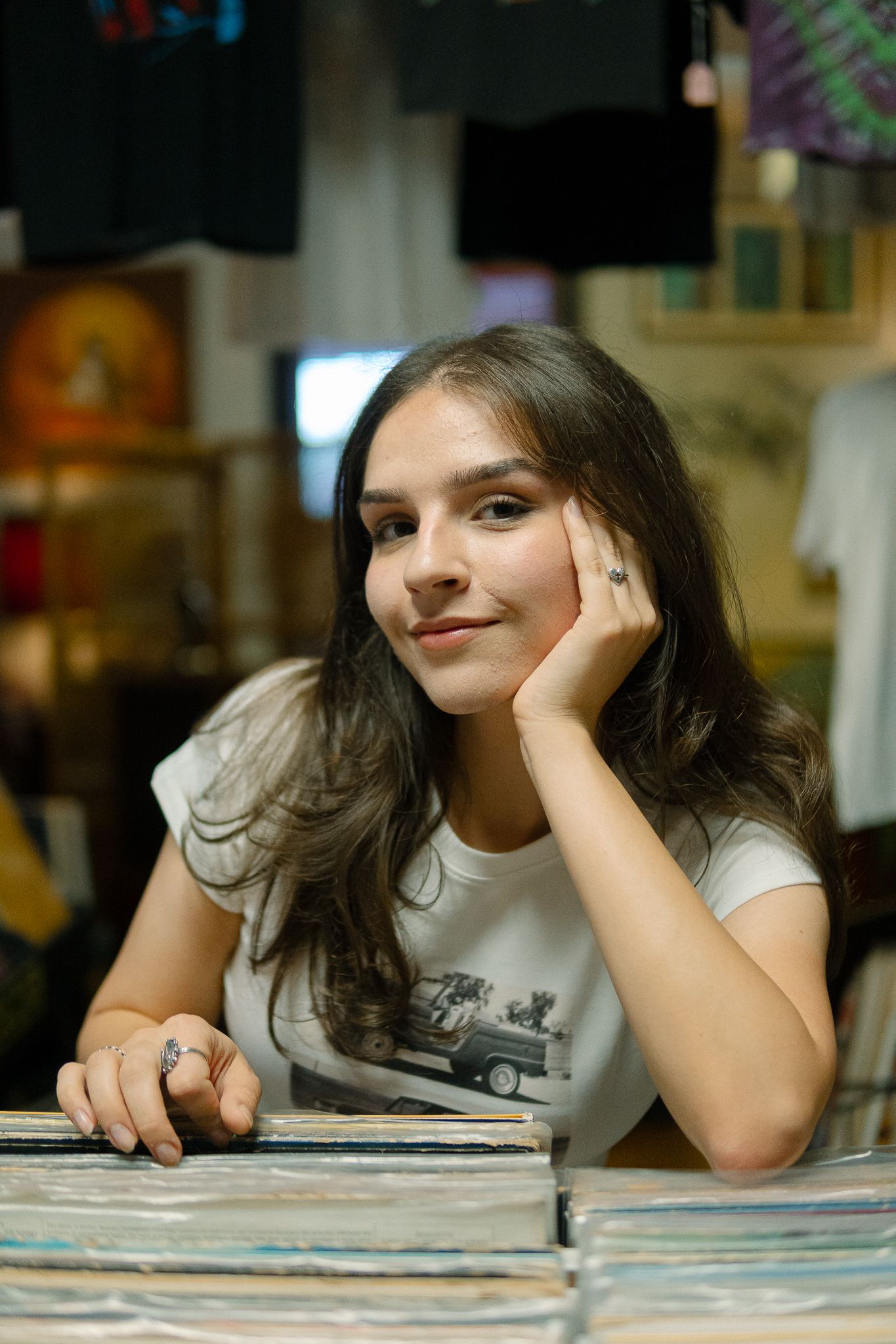 A person rests their head on their hand while looking at vinyl records laid out on a table in a store.