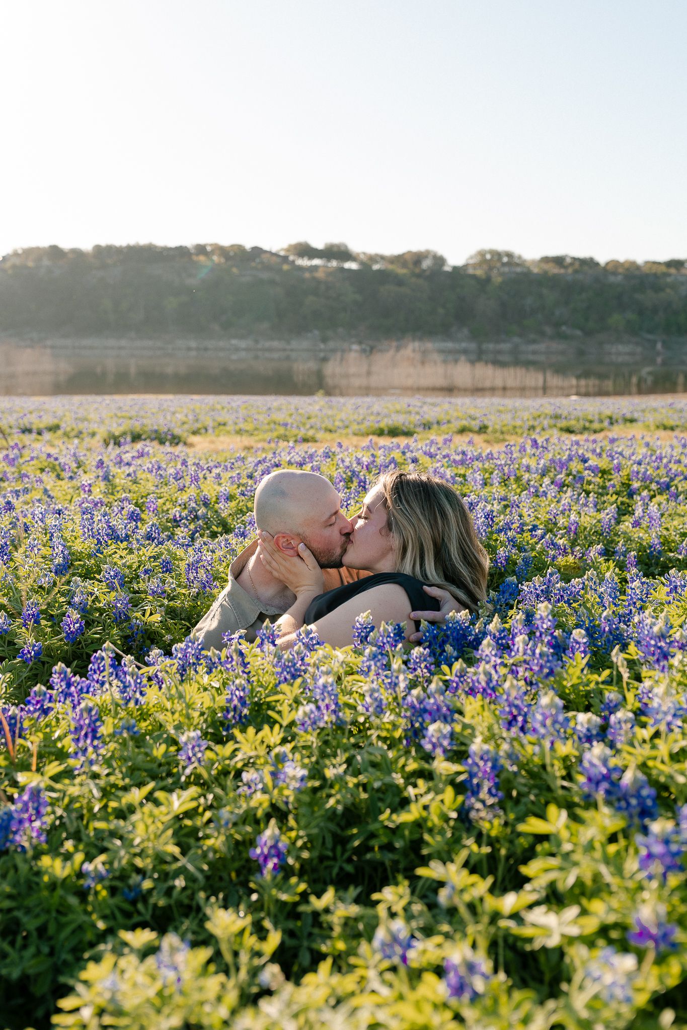 A couple shares a romantic moment among vibrant purple bluebonnets and yellow wildflowers in a Texas field at sunset.