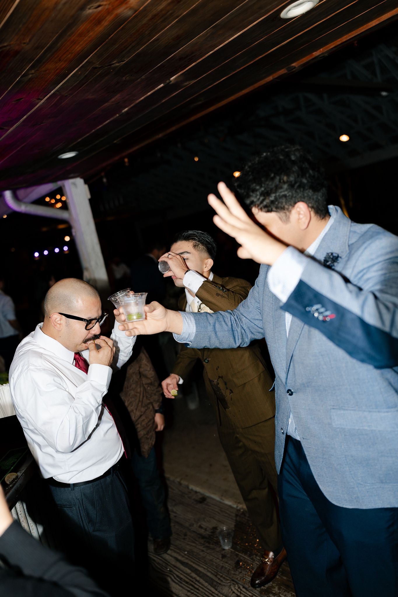 People dancing and celebrating at a dimly lit party venue with dramatic lighting effects.