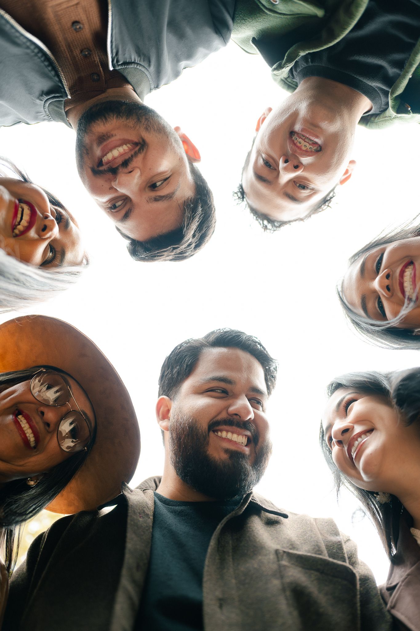 Low angle view of diverse smiling people forming a circle looking down at camera against white background.