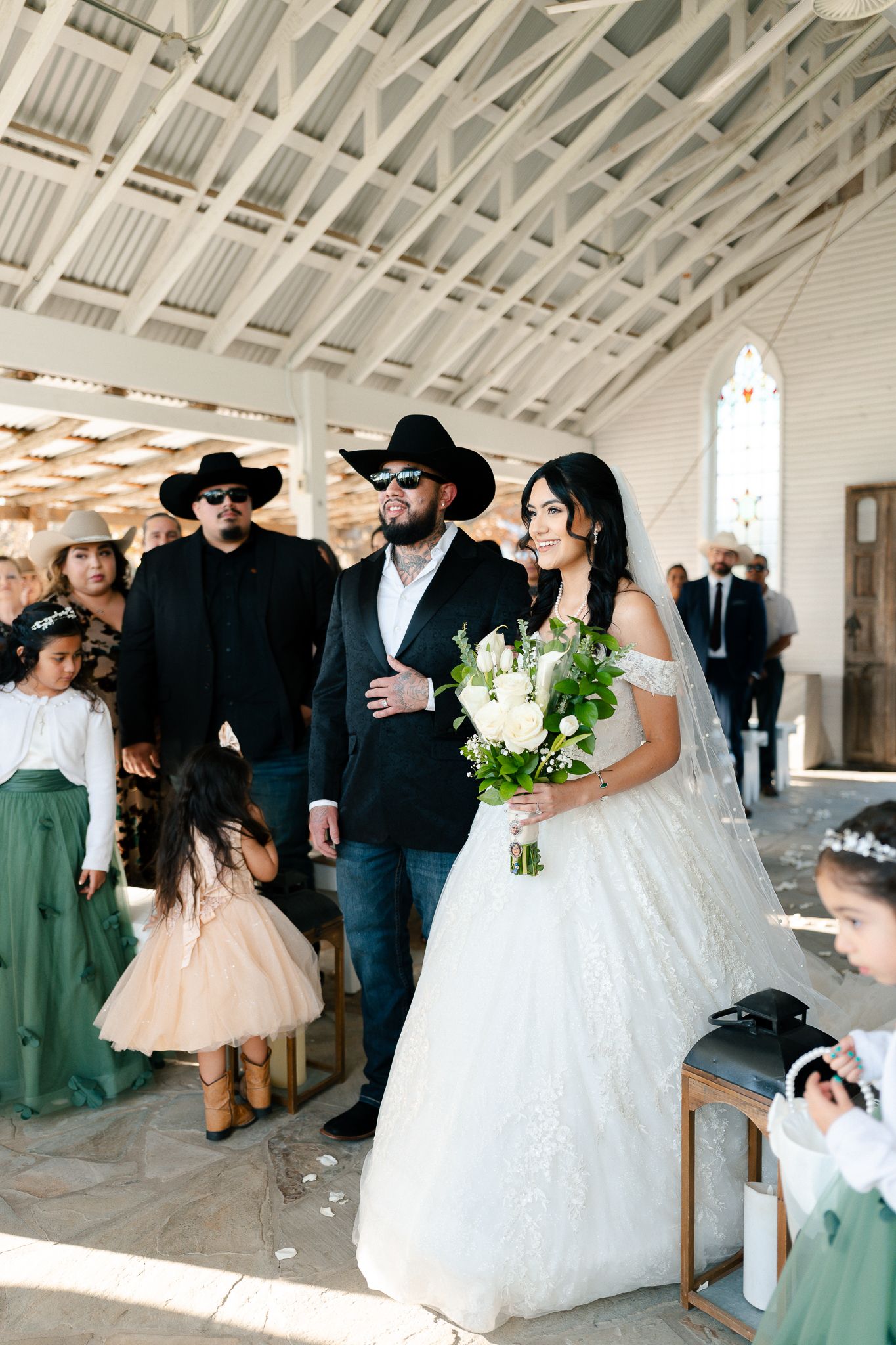 Wedding guests celebrate during a joyful reception moment in a bright white indoor venue with vaulted ceilings.