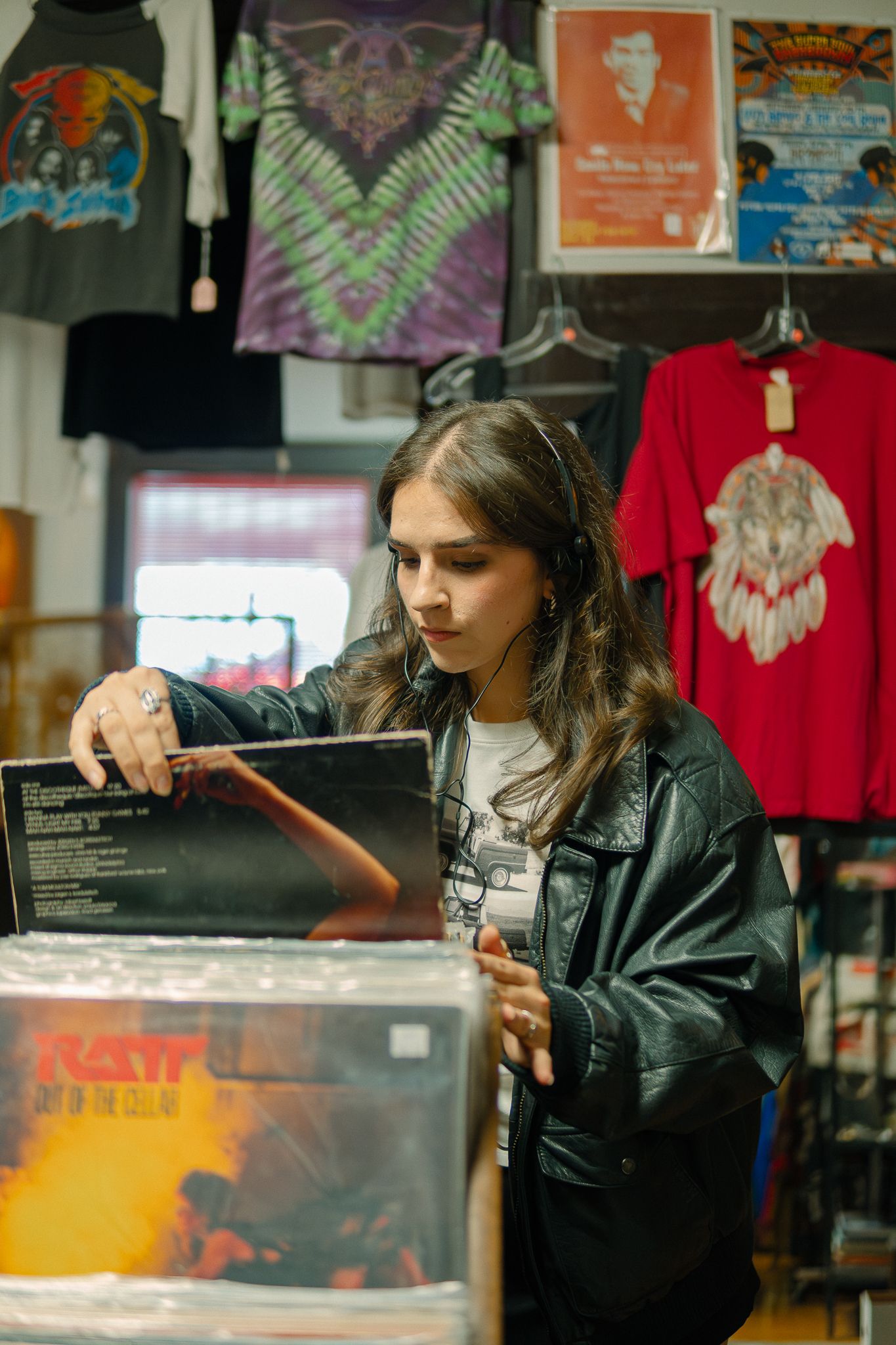 A customer browses through vinyl records in a retail shop with tie-dye shirts and posters displayed on the wall.