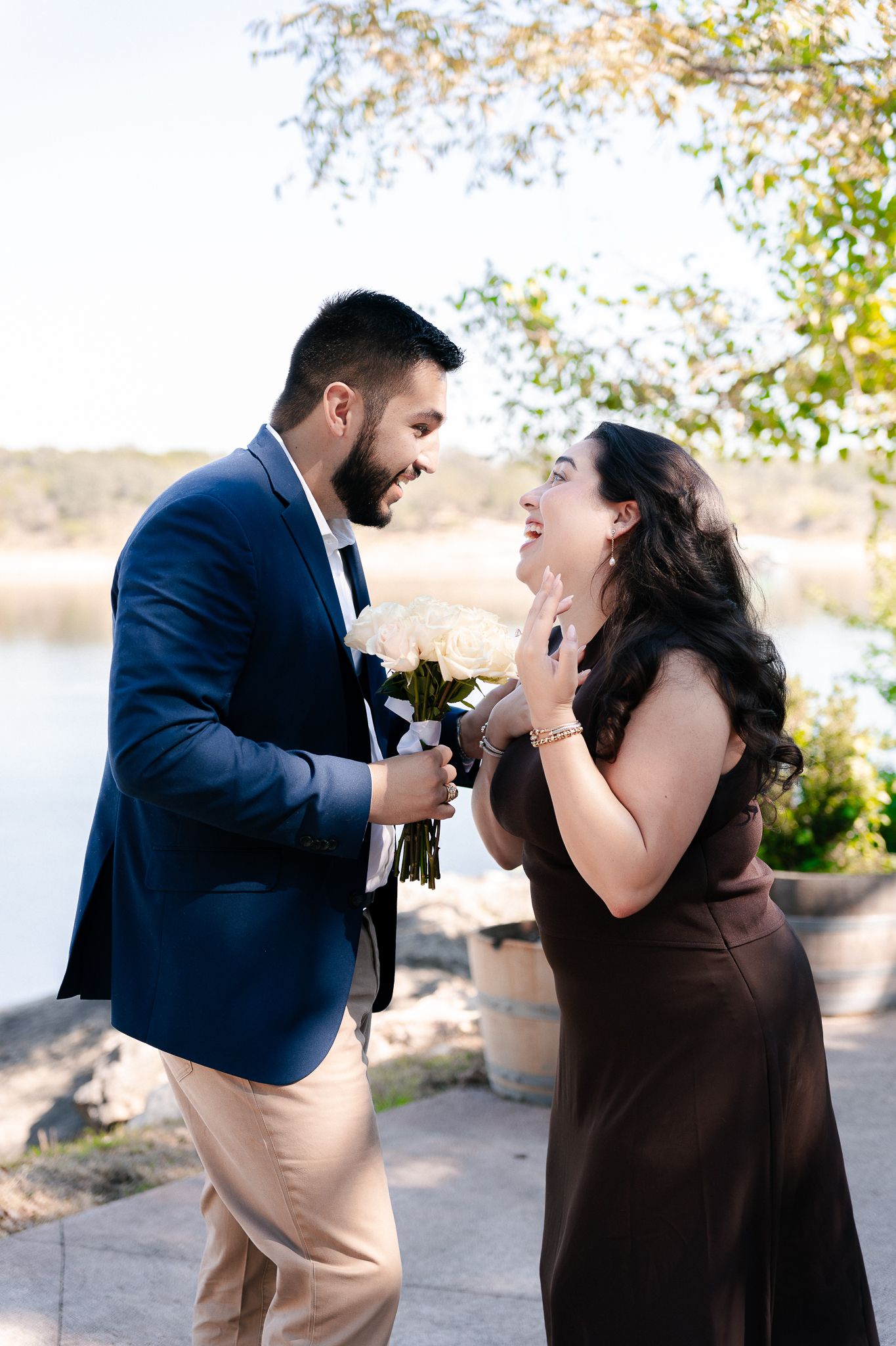 A couple in formal attire shares a playful moment while feeding each other cake outdoors during a special celebration.