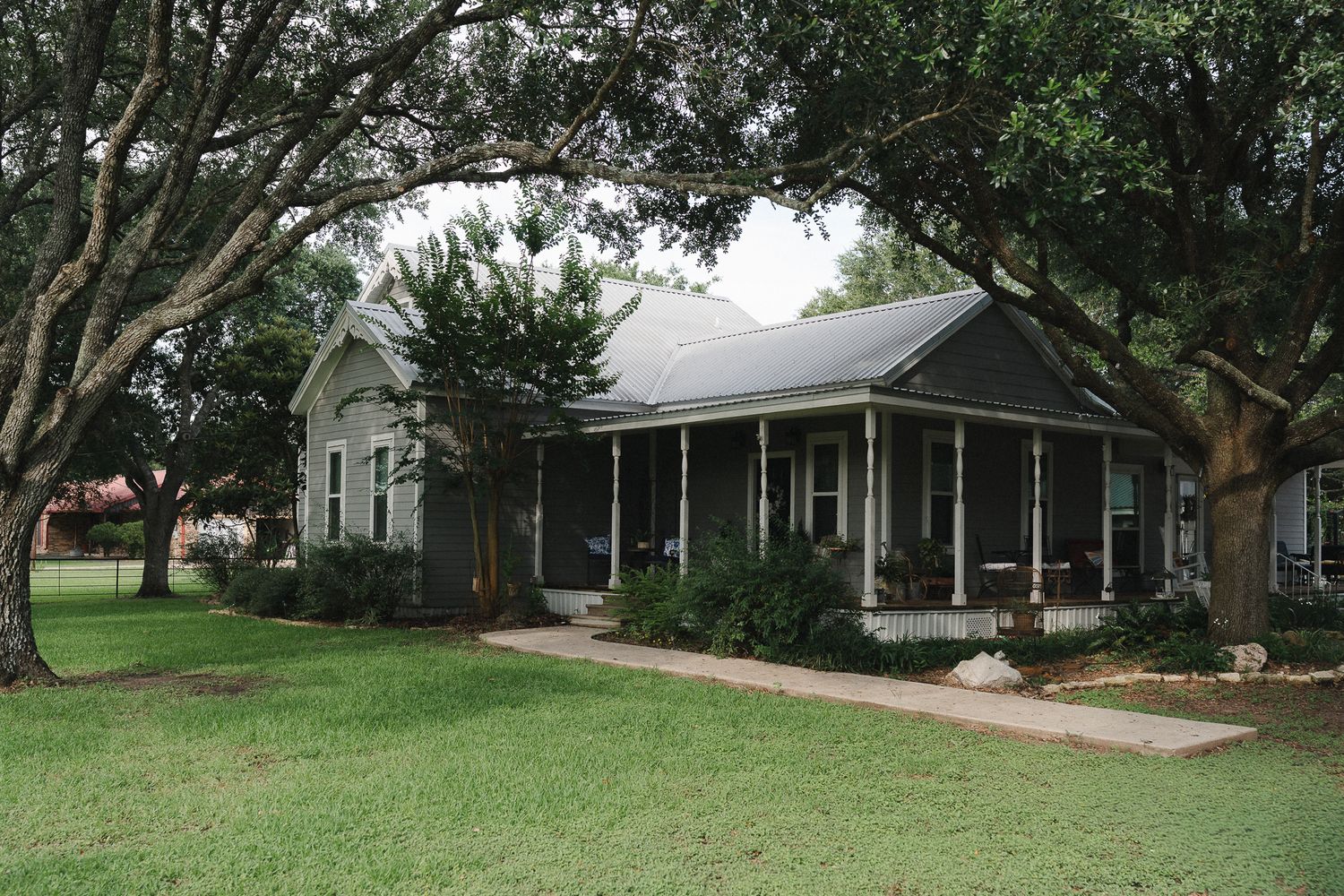 Charming Southern cottage with wrap-around porch surrounded by mature oak trees on a lush green lawn.