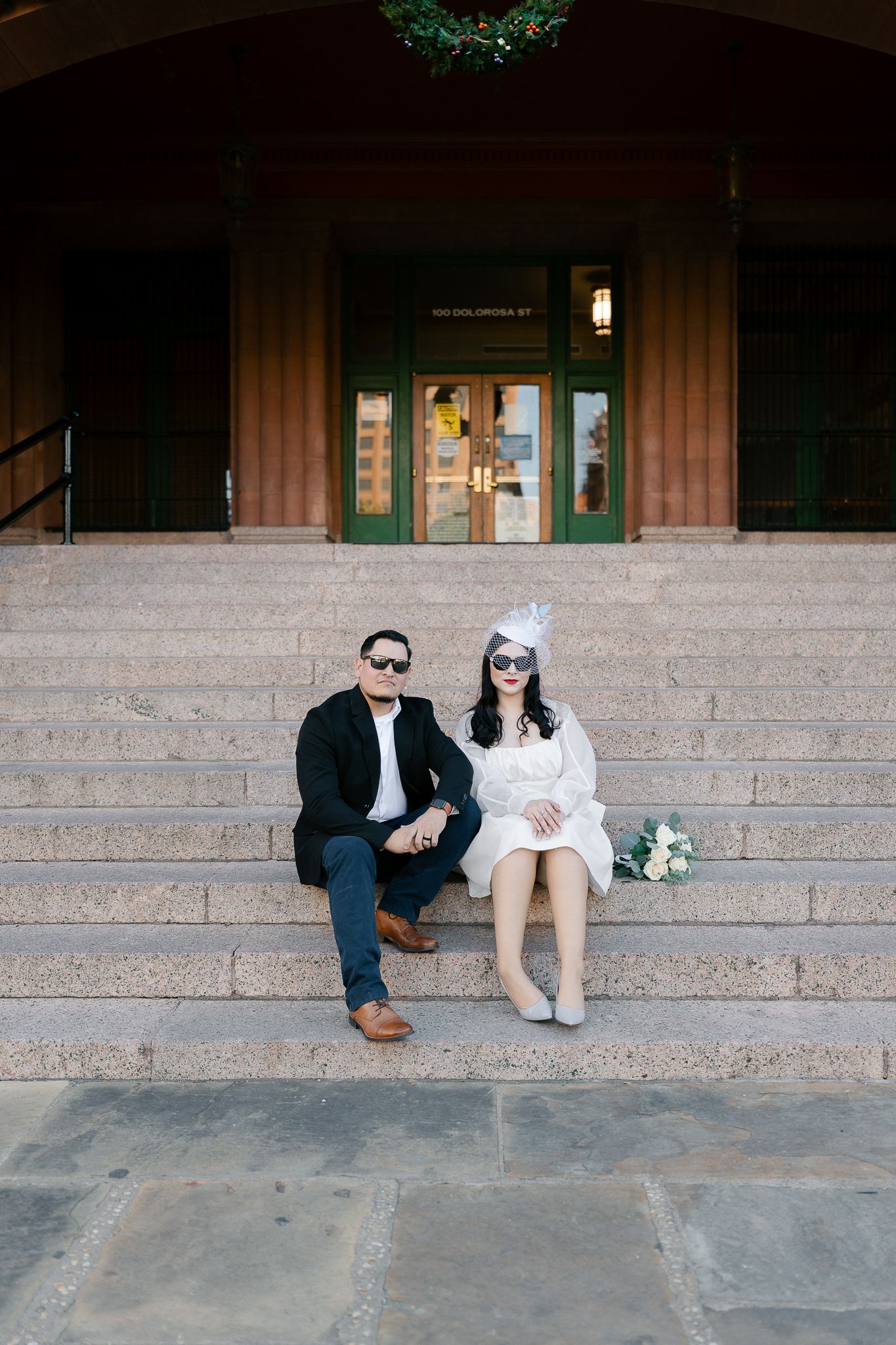 A couple sits together on stone steps outside a building with green trim windows in a series of four similar shots.