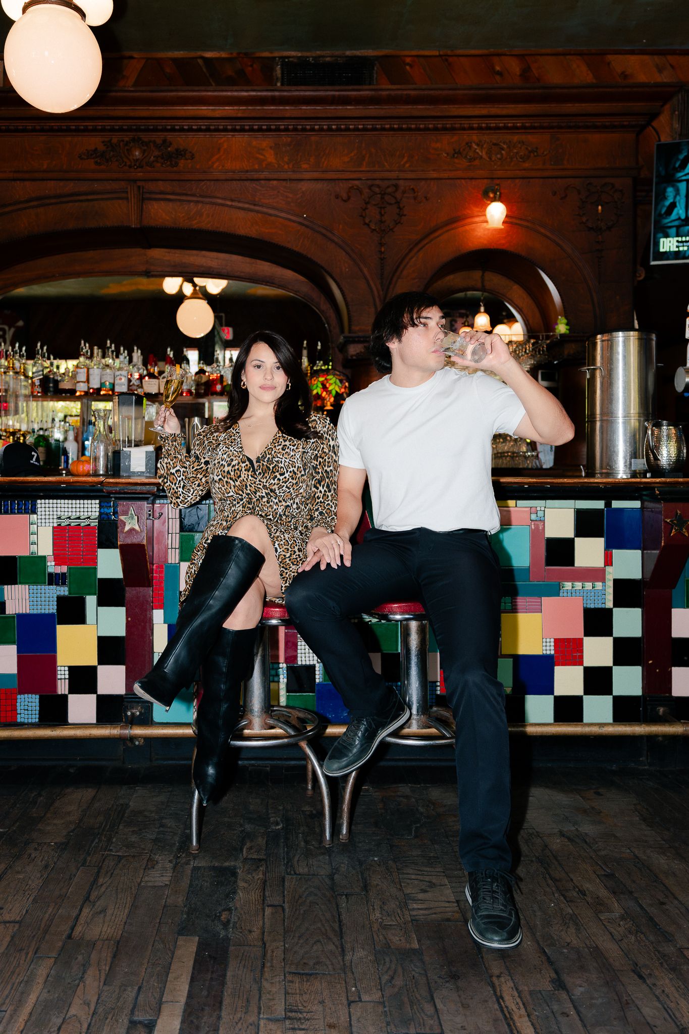 A sequence of dance moves shown across five frames on a wooden floor against a colorful tiled wall in a bar setting.