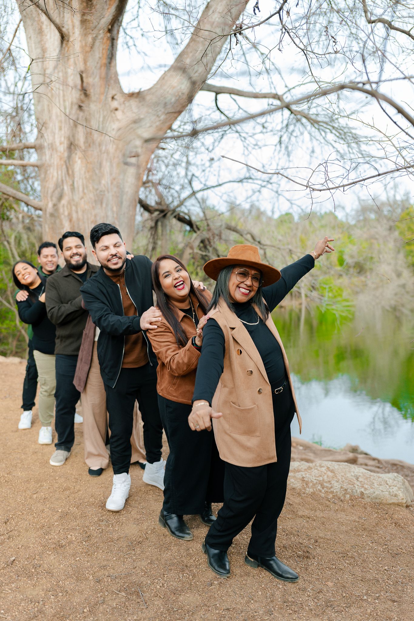 A group of friends pose playfully by a lake on a winter day, creating a fun domino-effect photo sequence.