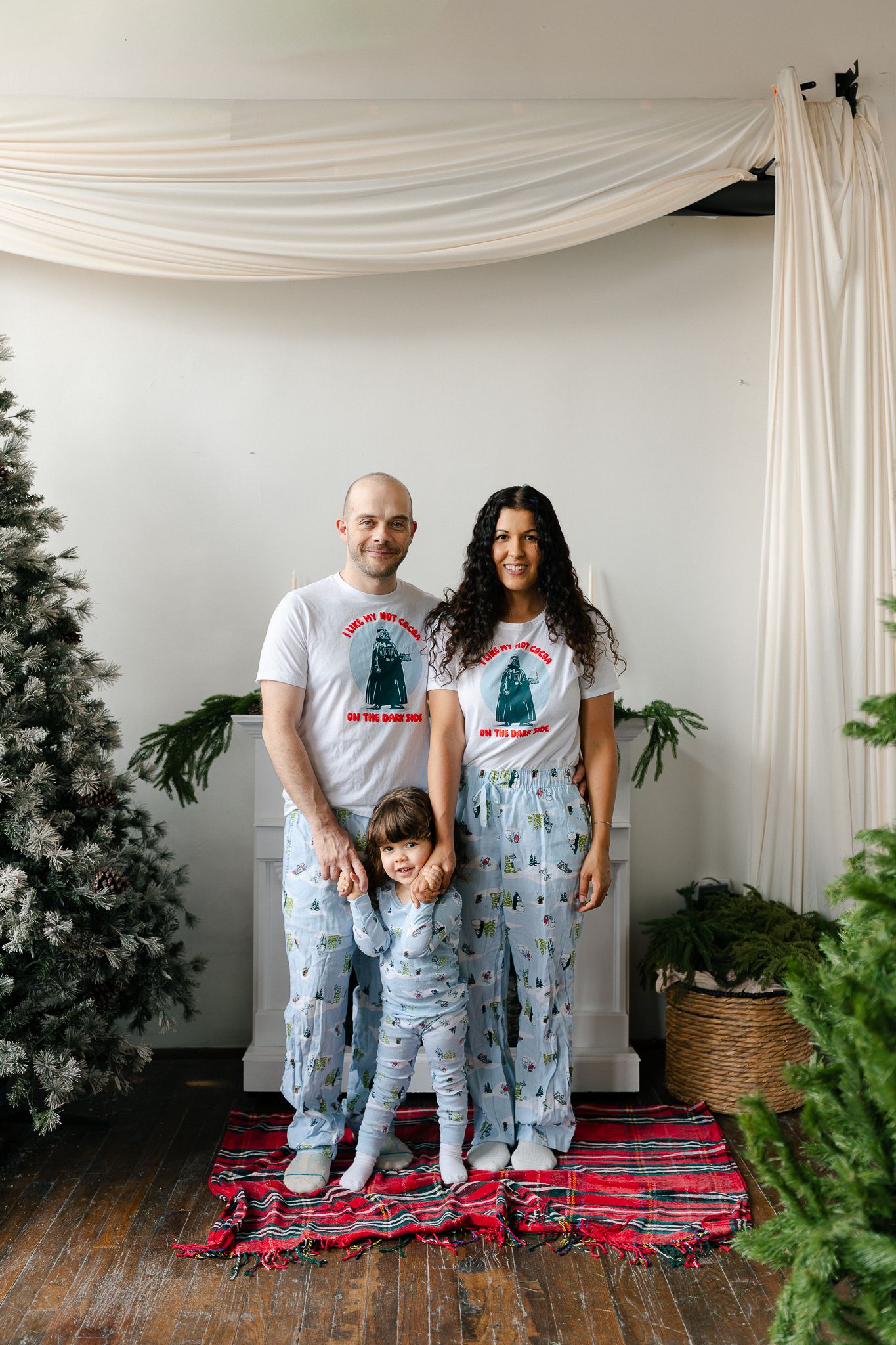 A family poses together in matching winter pajamas with festive prints against a white backdrop and red striped rug.