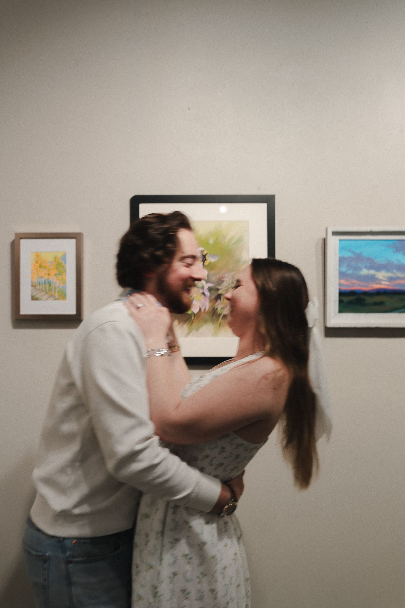 Couple sharing a romantic moment in an art gallery with framed paintings on the wall behind them.