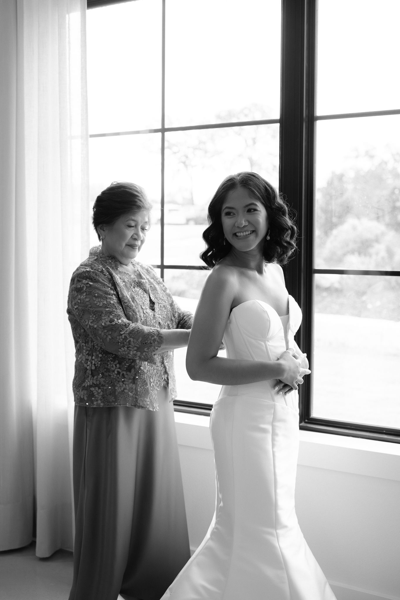 Black and white photo sequence showing someone getting dressed in a white wedding gown near bright windows.