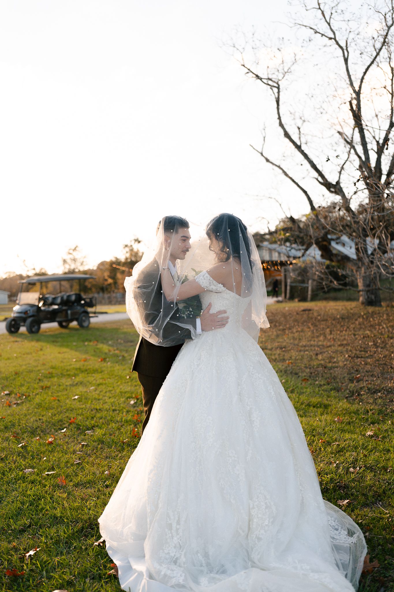 Bride and groom share romantic moment under veil outdoors at golden hour wedding ceremony.