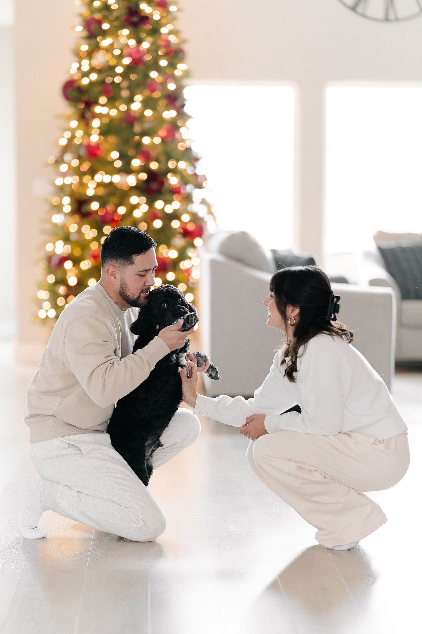 Photographers in white outfits capture holiday photos in front of decorated Christmas trees in a bright studio setting.