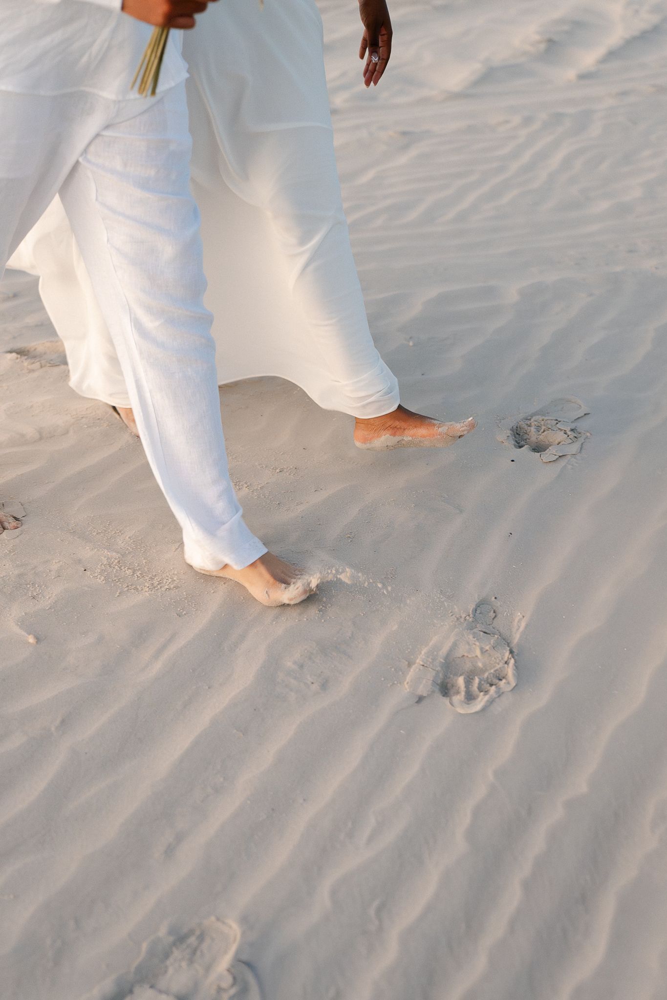 Bare feet walking in soft white sand leaving footprints along a pristine beach.
