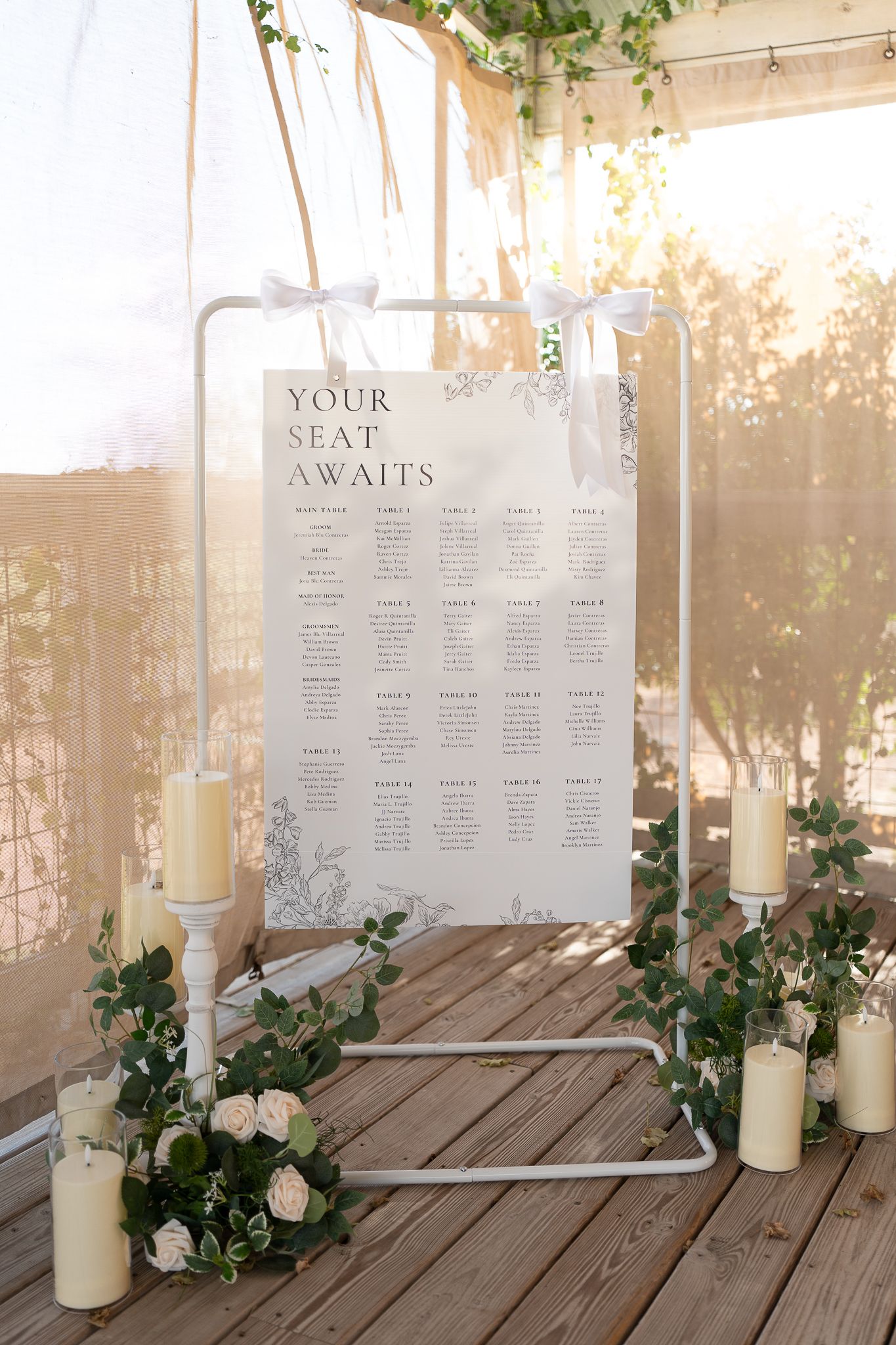 Wedding seating chart display with white candles and greenery garland on rustic wooden table in natural light.