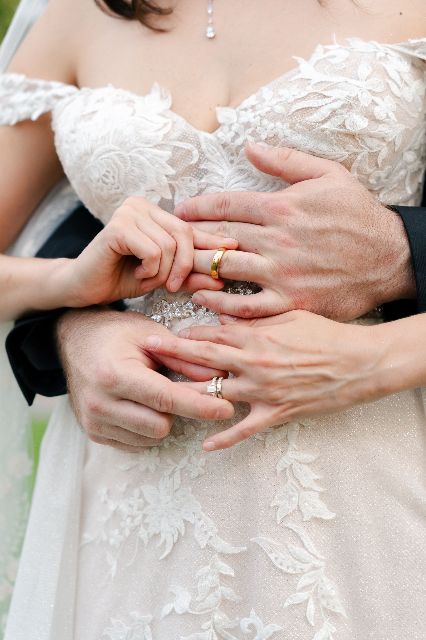 A series of hands exchanging wedding rings against a white lace dress background during a wedding ceremony.