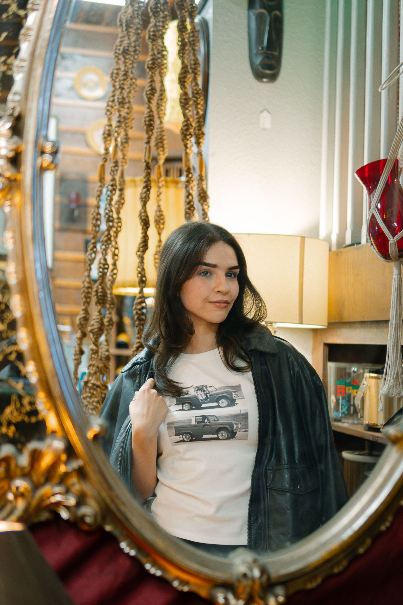 Mirror reflection shows person in white t-shirt and black jacket sitting in elegant room with gold accents and lighting.