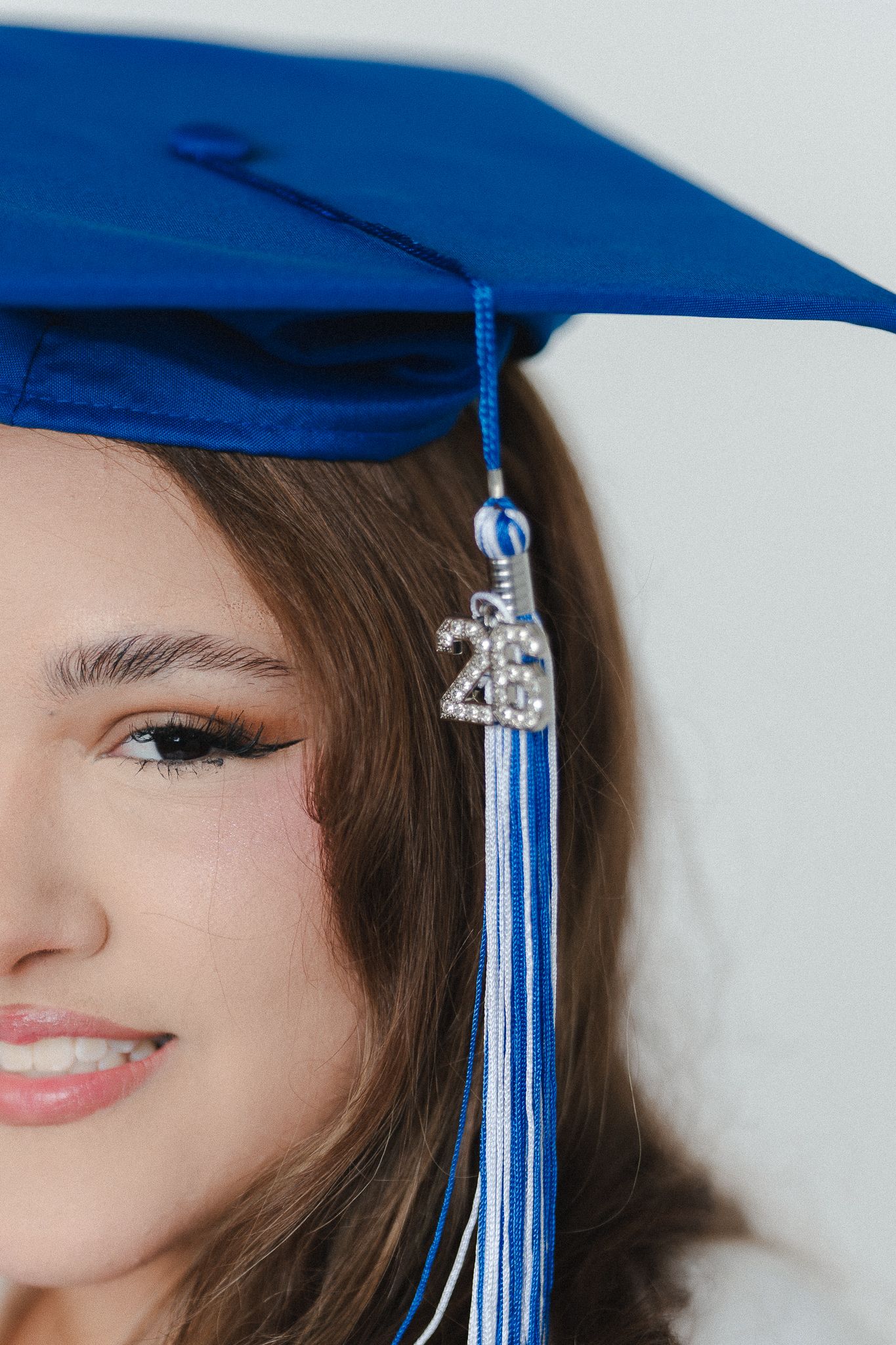 Young woman wearing a blue graduation cap with tassel and 2023 charm, smiling against white background.