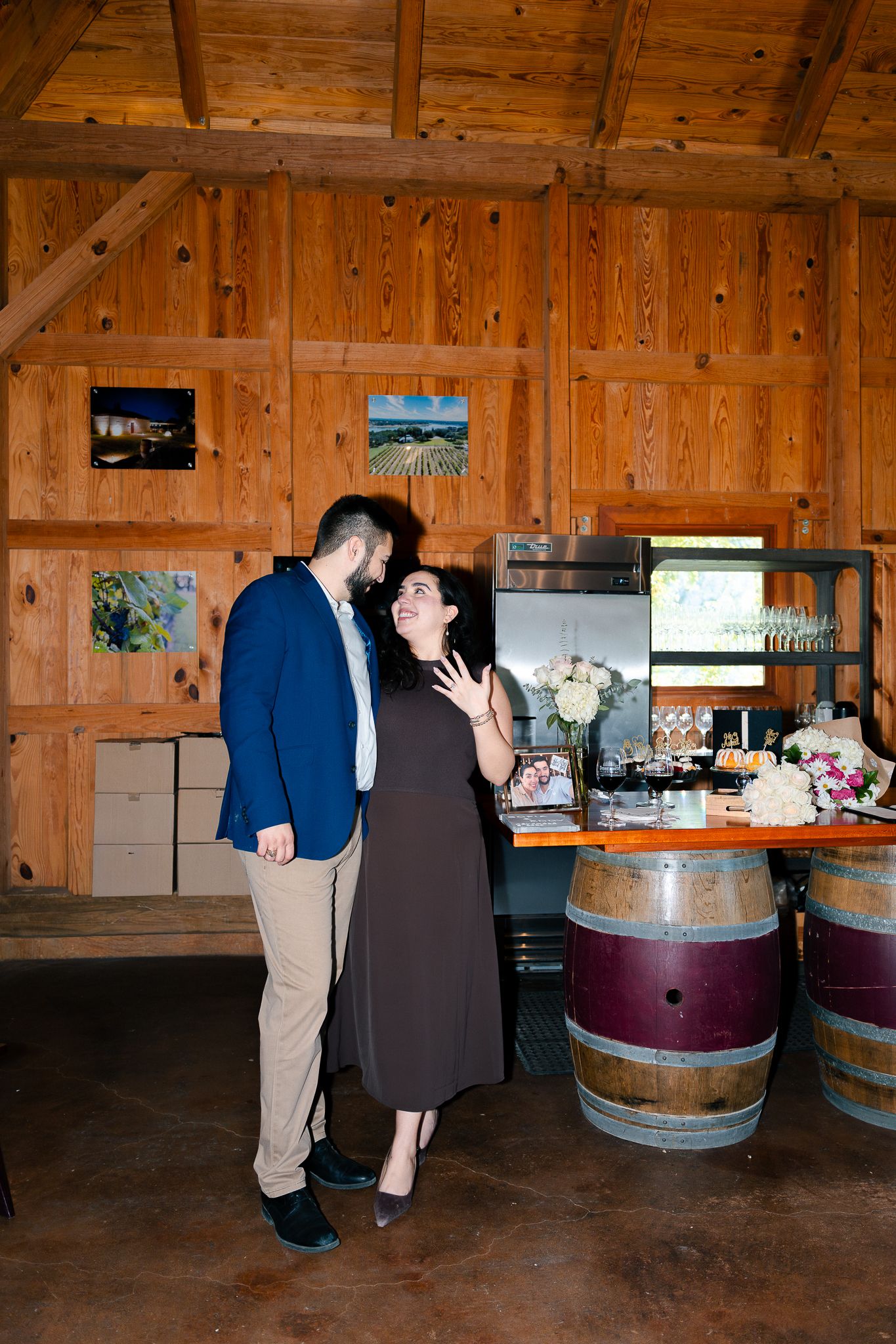 Rustic wooden barn interior with wine barrel tables and decorative floral arrangements.
